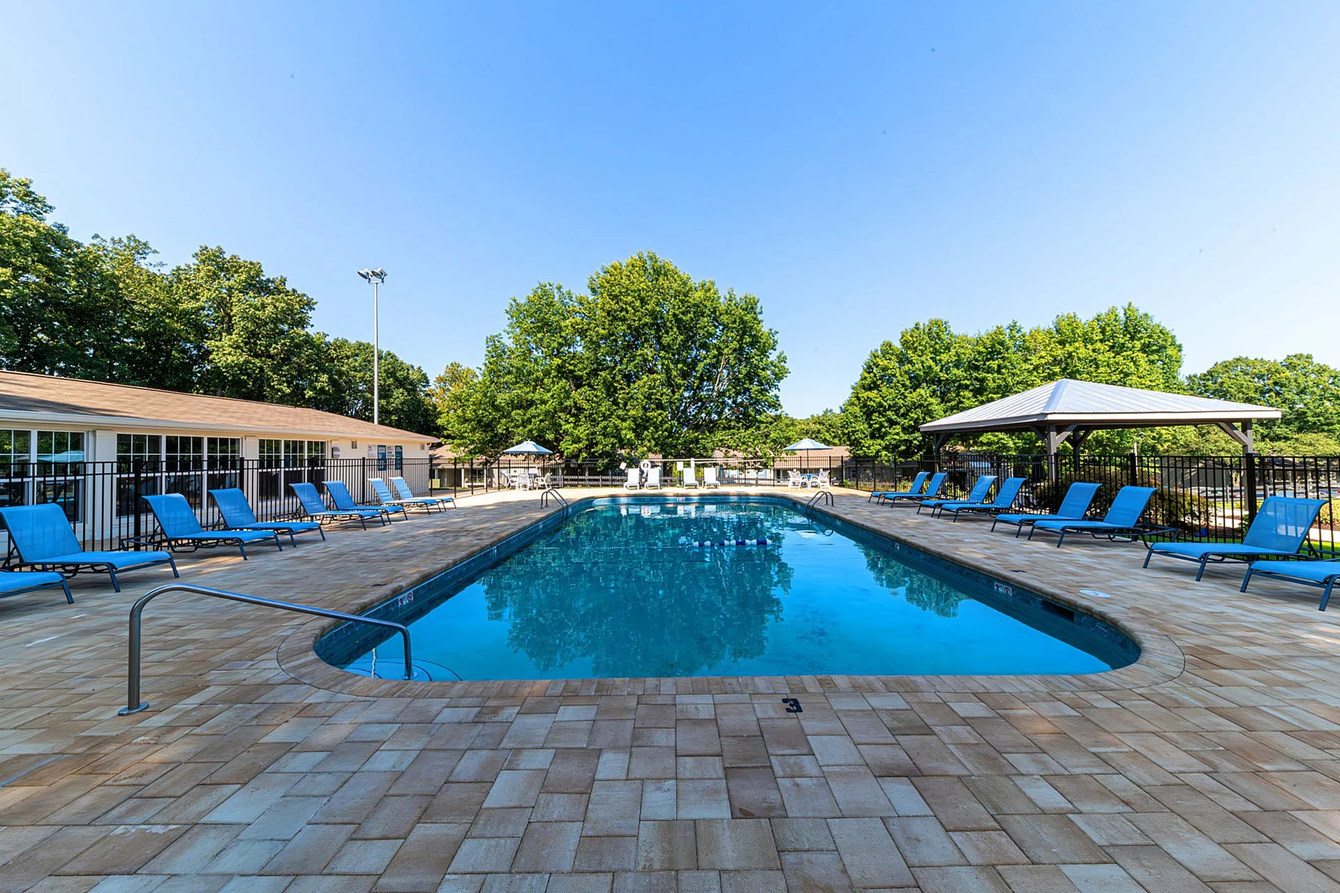 Inviting outdoor pool area with sleek lounge chairs, surrounded by lush greenery and shaded pavilions.
