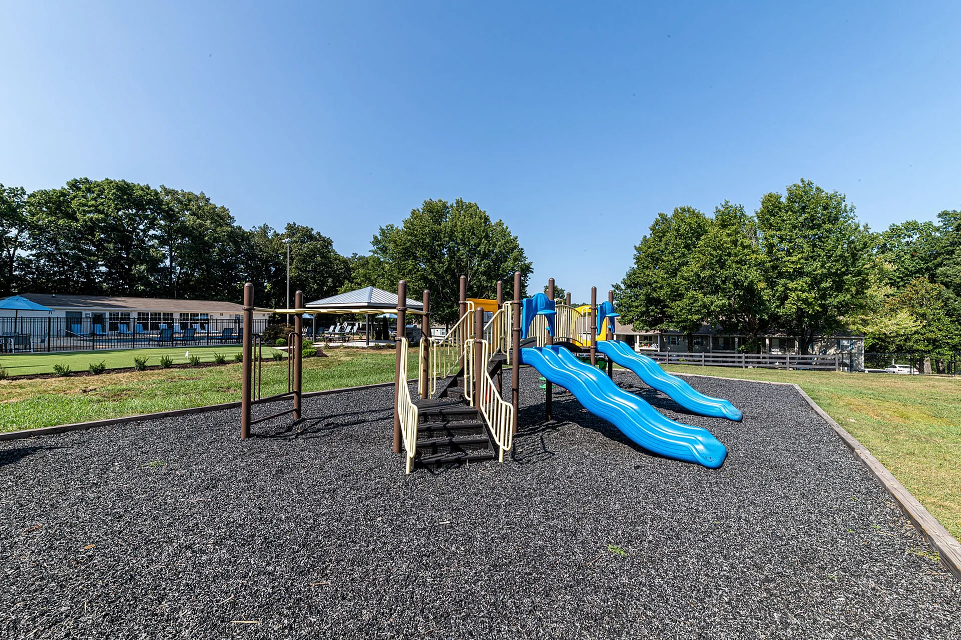 Inviting playground with vibrant blue slides and a sturdy climbing structure, surrounded by scenic greenery, perfect for family enjoyment.