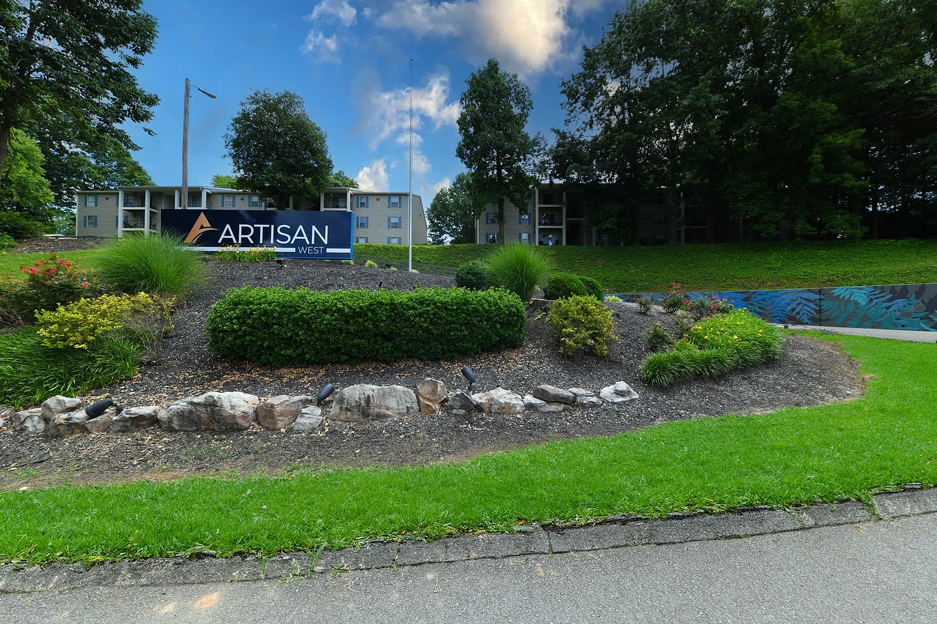 Inviting apartment complex surrounded by lush greenery and colorful landscaping, highlighted by a chic Artisan West entrance sign.