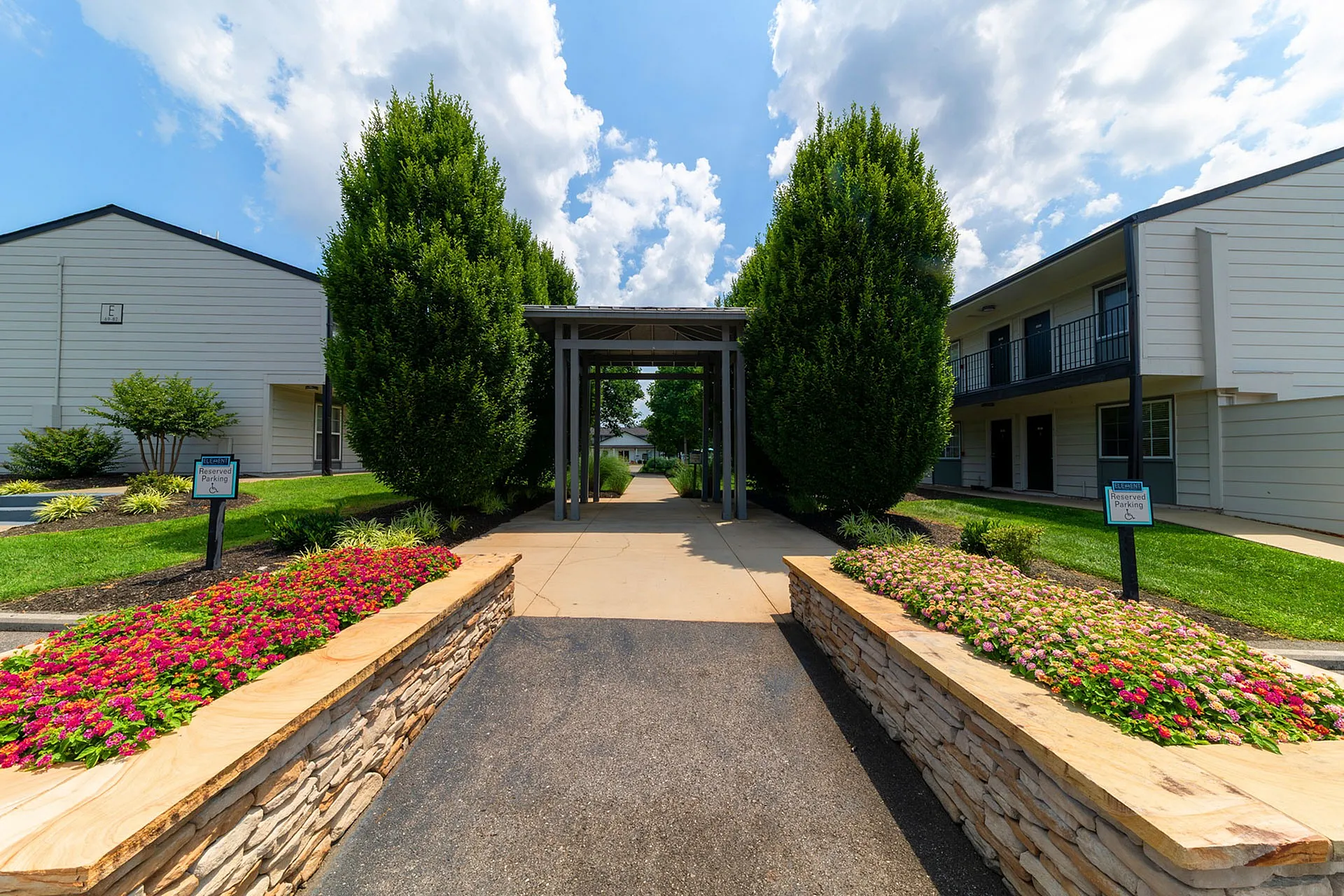 Charming apartment entrance with a lush landscaped path, vibrant flower beds, and modern architecture.