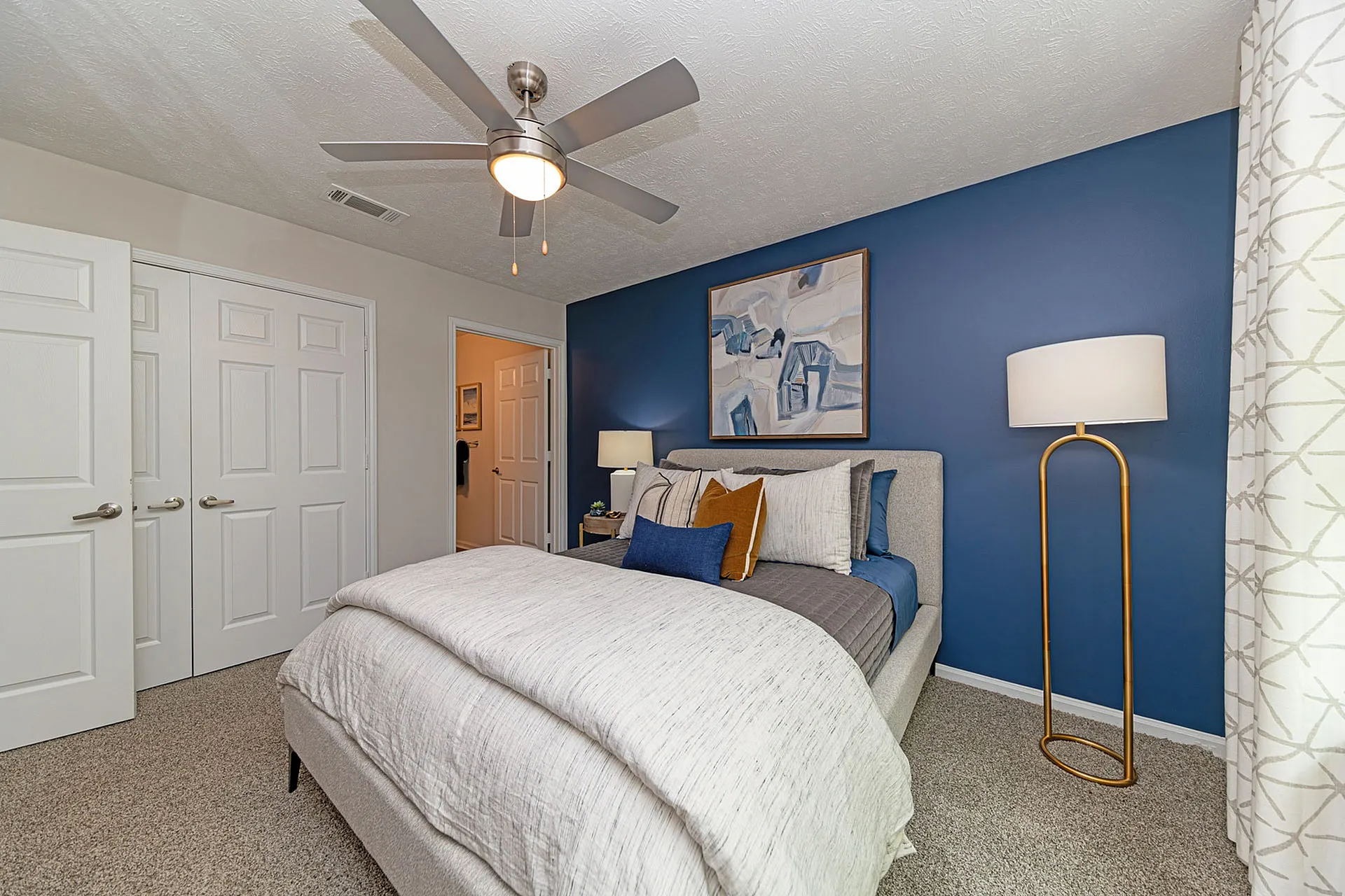 Elegant bedroom with a cozy bed, modern ceiling fan, and stylish blue accent wall featuring contemporary art.