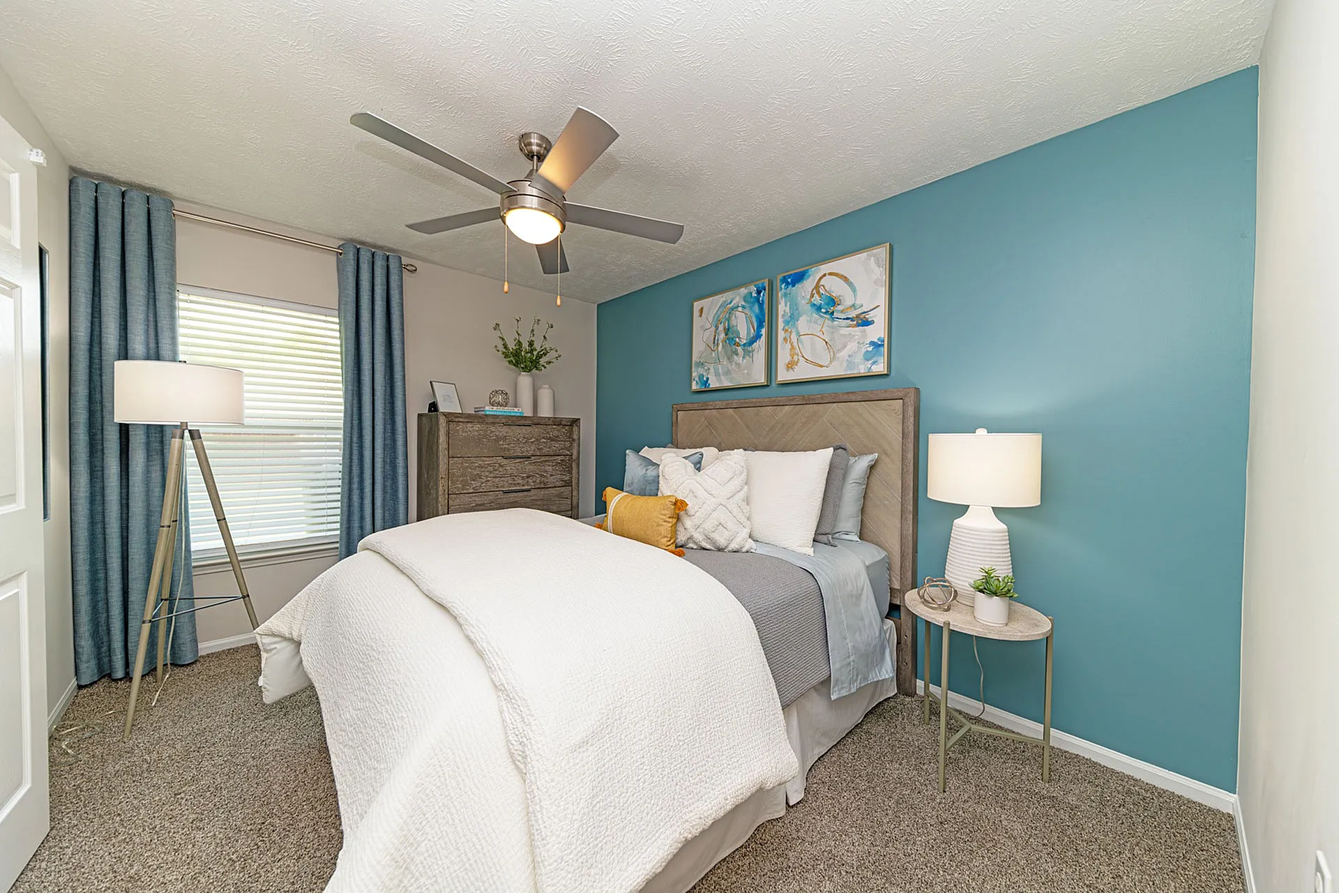 Inviting bedroom with soothing teal accent wall, modern ceiling fan, cozy bed with plush pillows, and elegant decor for a relaxing ambience.