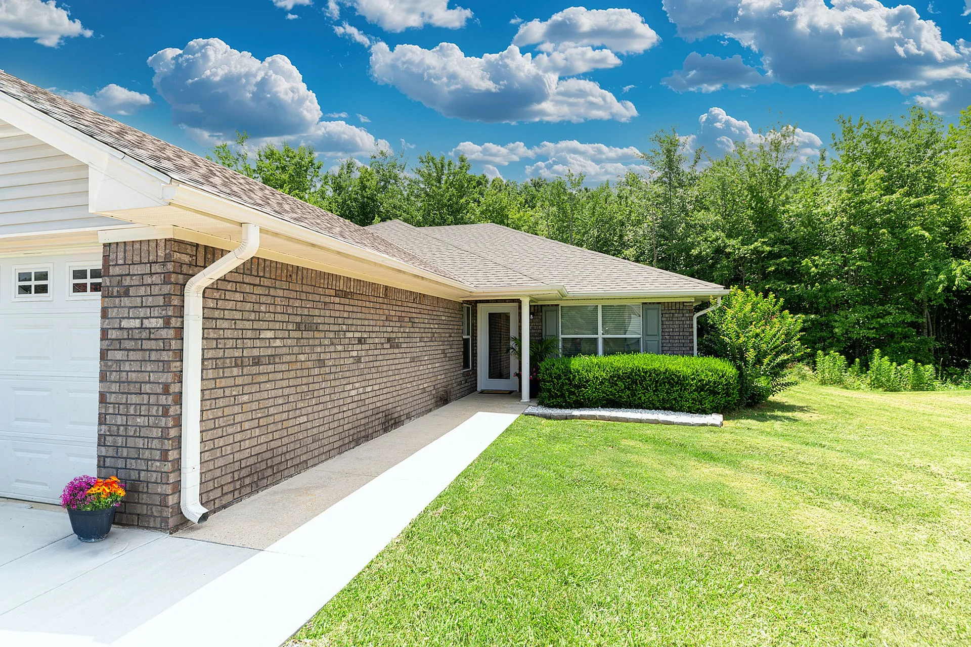 Charming brick house with lush green lawn, vibrant flowers, and a sunny blue sky backdrop.