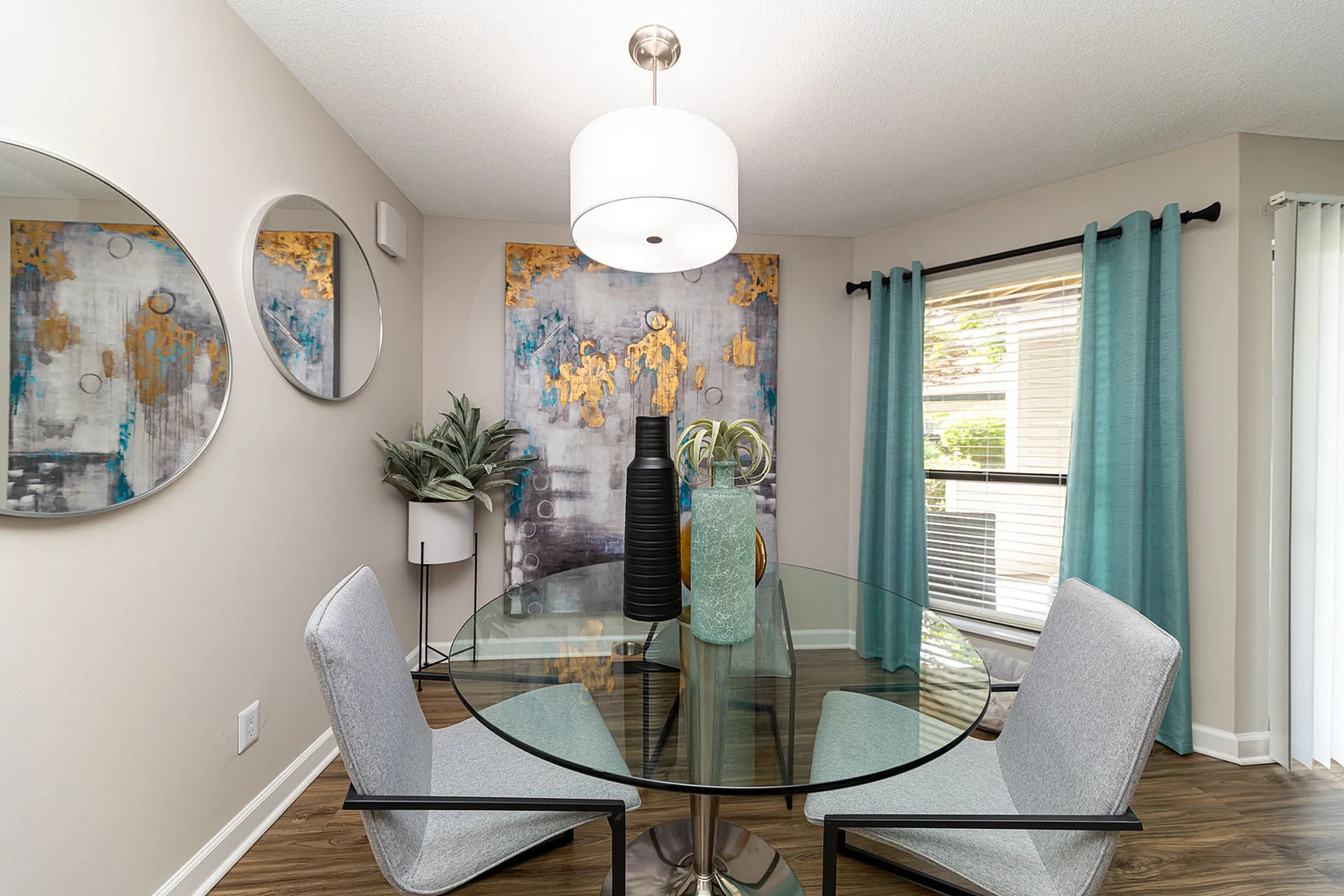 Elegant dining area with modern glass table and abstract artwork, featuring chic decor and large windows for natural light.