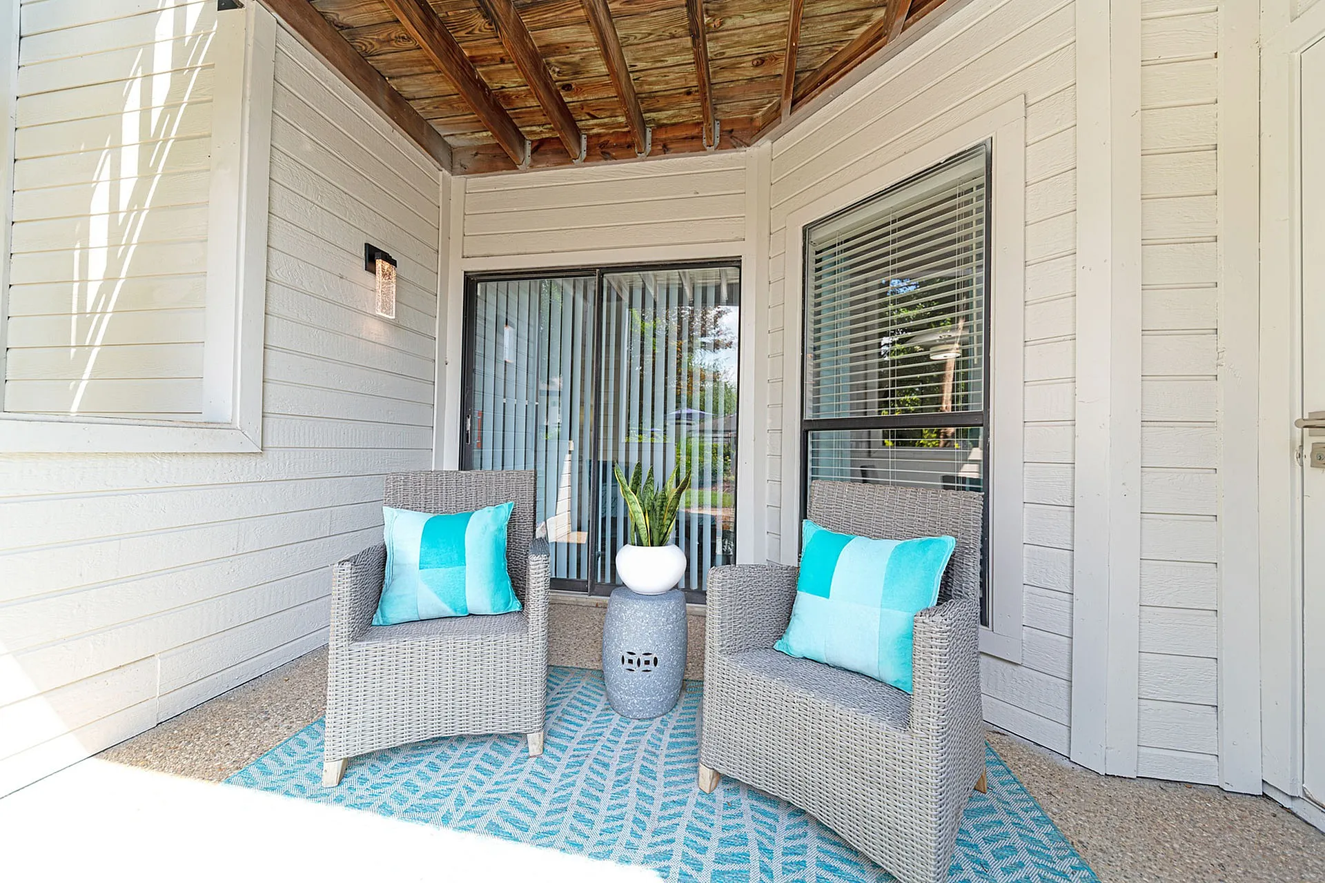 Charming outdoor patio featuring two stylish wicker chairs with turquoise cushions, a modern side table, and lush greenery creating a serene retreat.