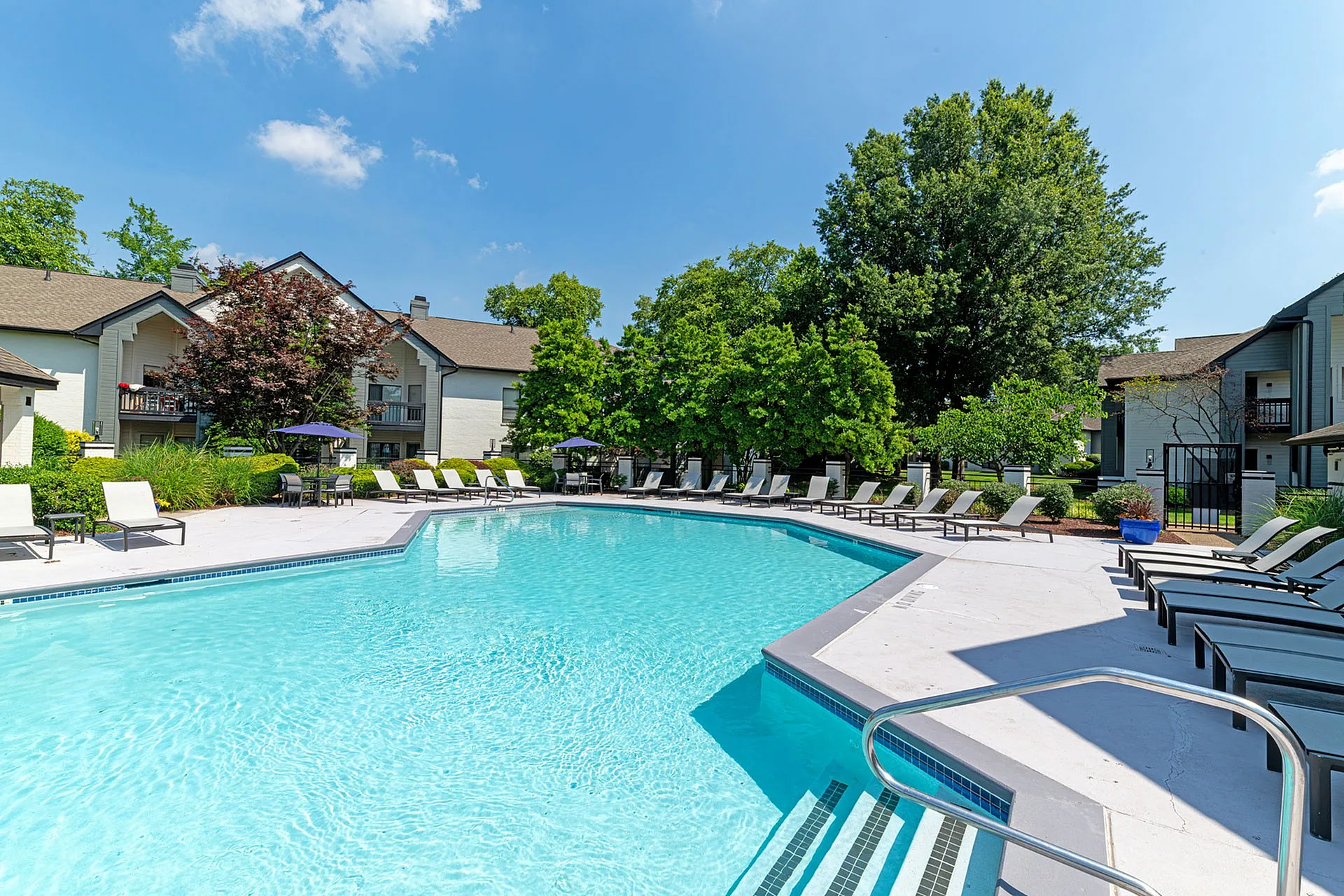 Luxurious apartment community showcasing a pristine swimming pool with elegant lounge chairs surrounded by lush green trees.