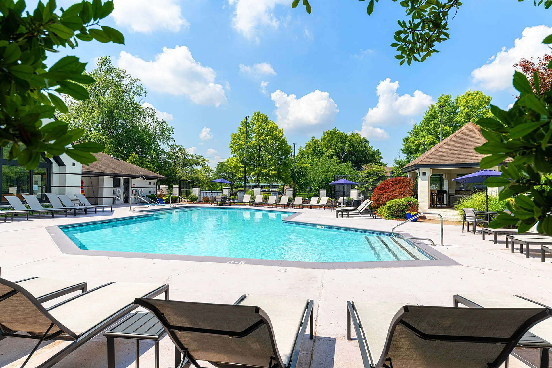 Inviting outdoor pool area with comfortable lounge chairs, surrounded by lush greenery and a clear blue sky, perfect for relaxation and leisure.