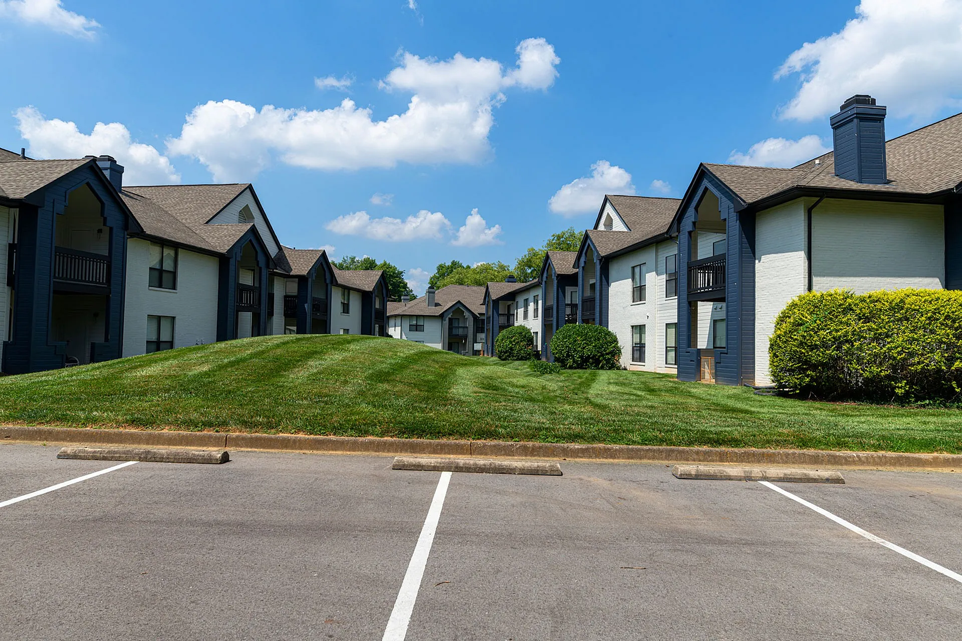 Charming apartment complex with modern architecture, lush green lawns, and bright blue skies, offering a welcoming and serene living environment.