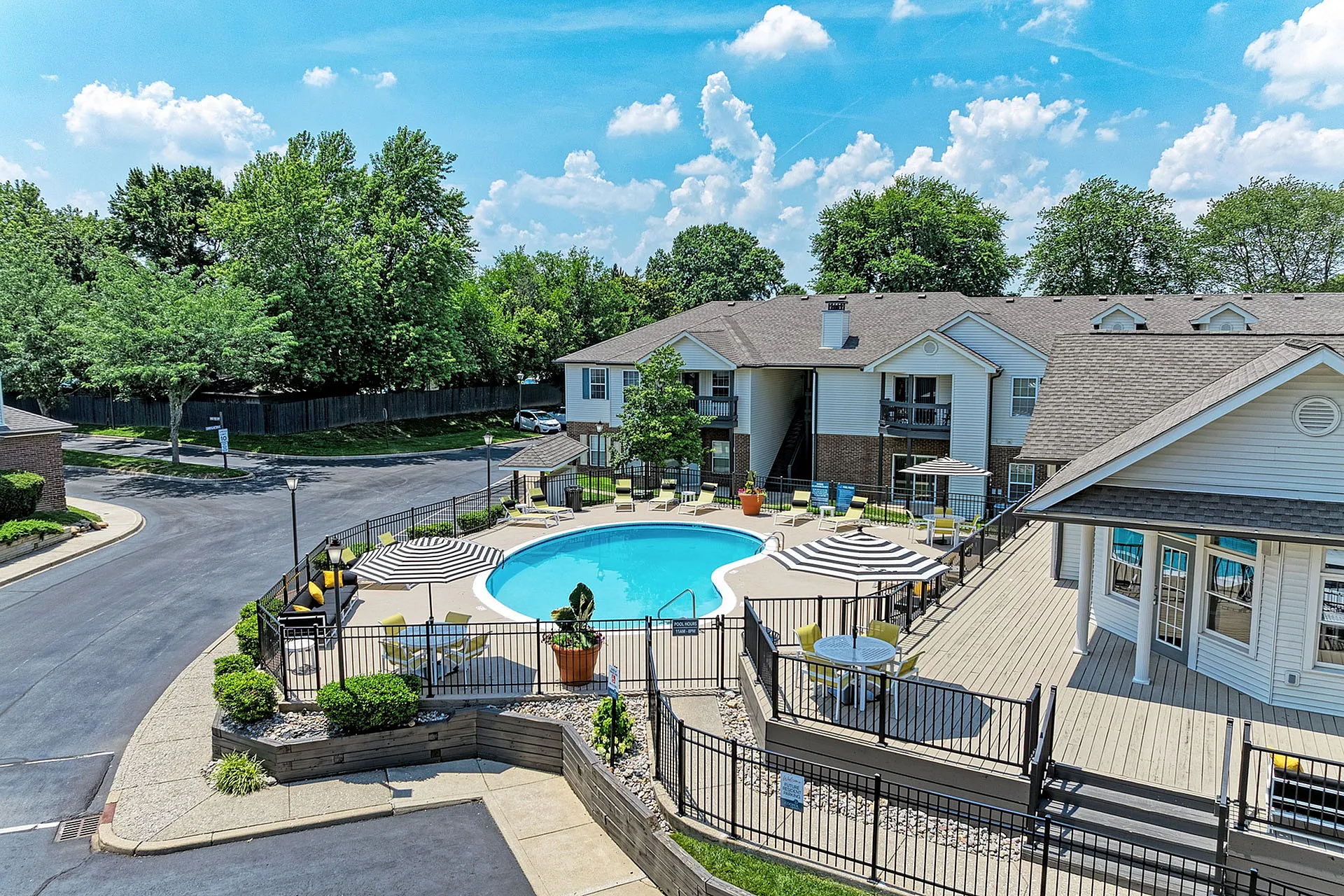 Charming apartment community with stunning outdoor pool, elegant seating areas, and lush green surroundings under a bright blue sky.