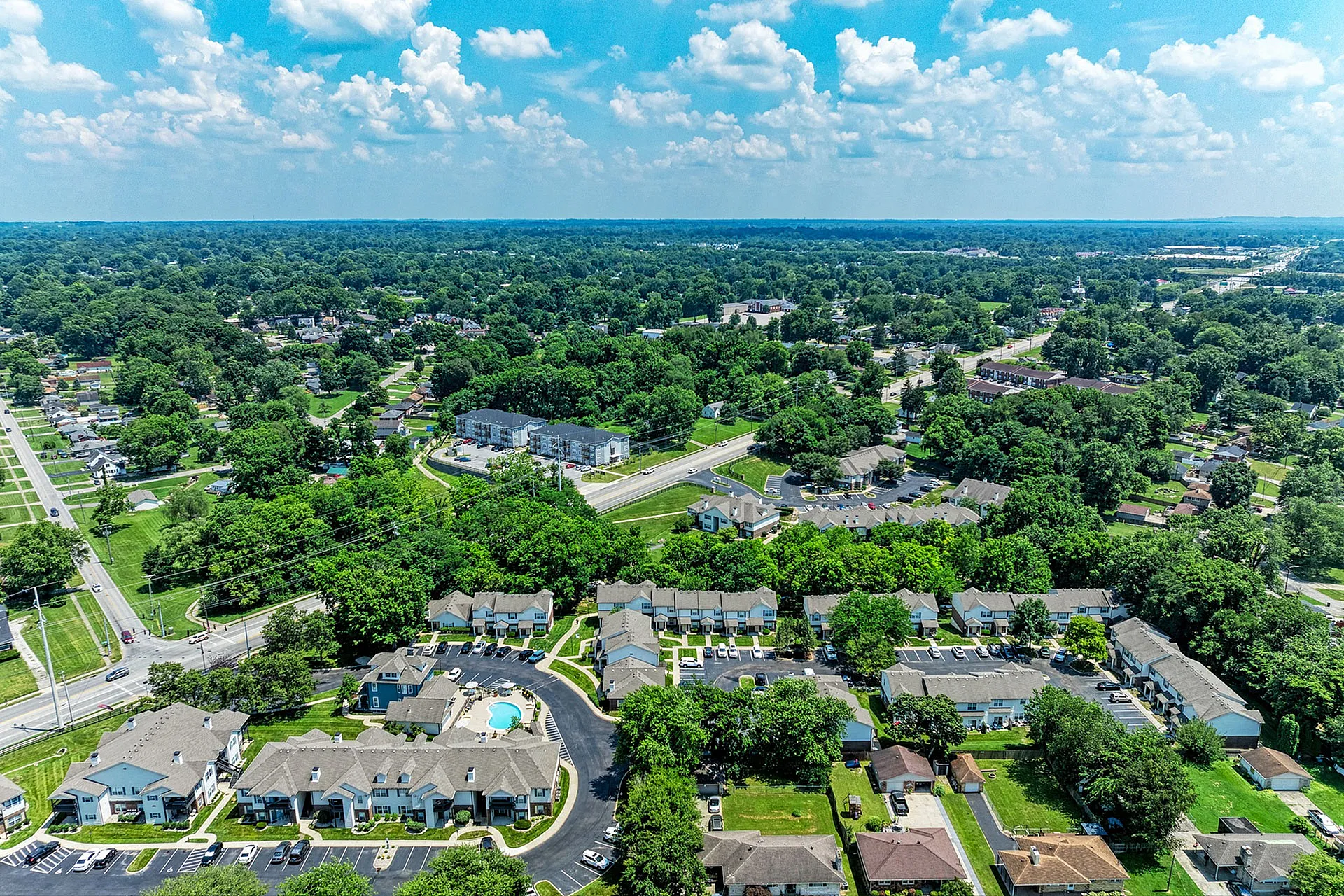Vibrant aerial view of a picturesque suburban neighborhood featuring a charming residential complex with a sparkling central pool, nestled amid lush greenery.