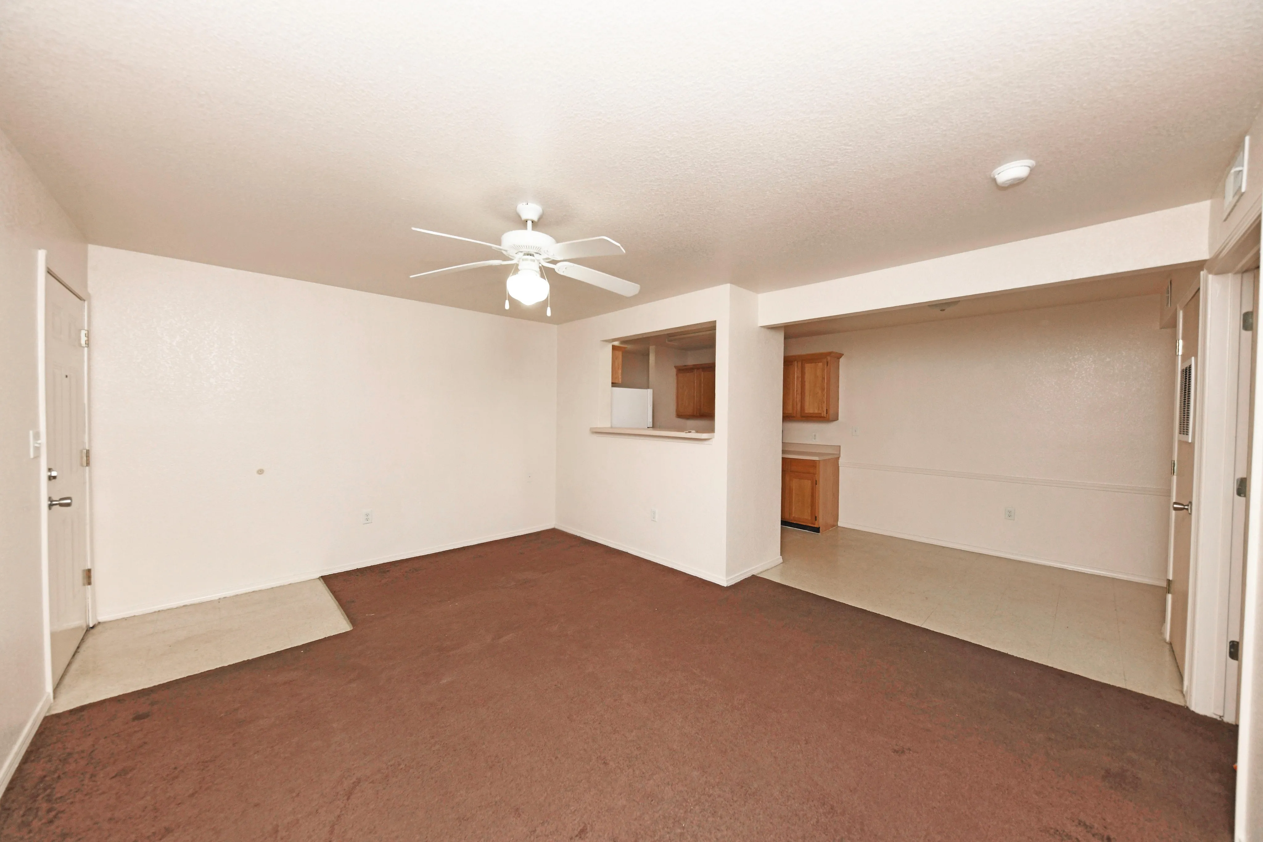 Bright living space with ceiling fan, open view to kitchen featuring wooden cabinets, and welcoming brown carpet.