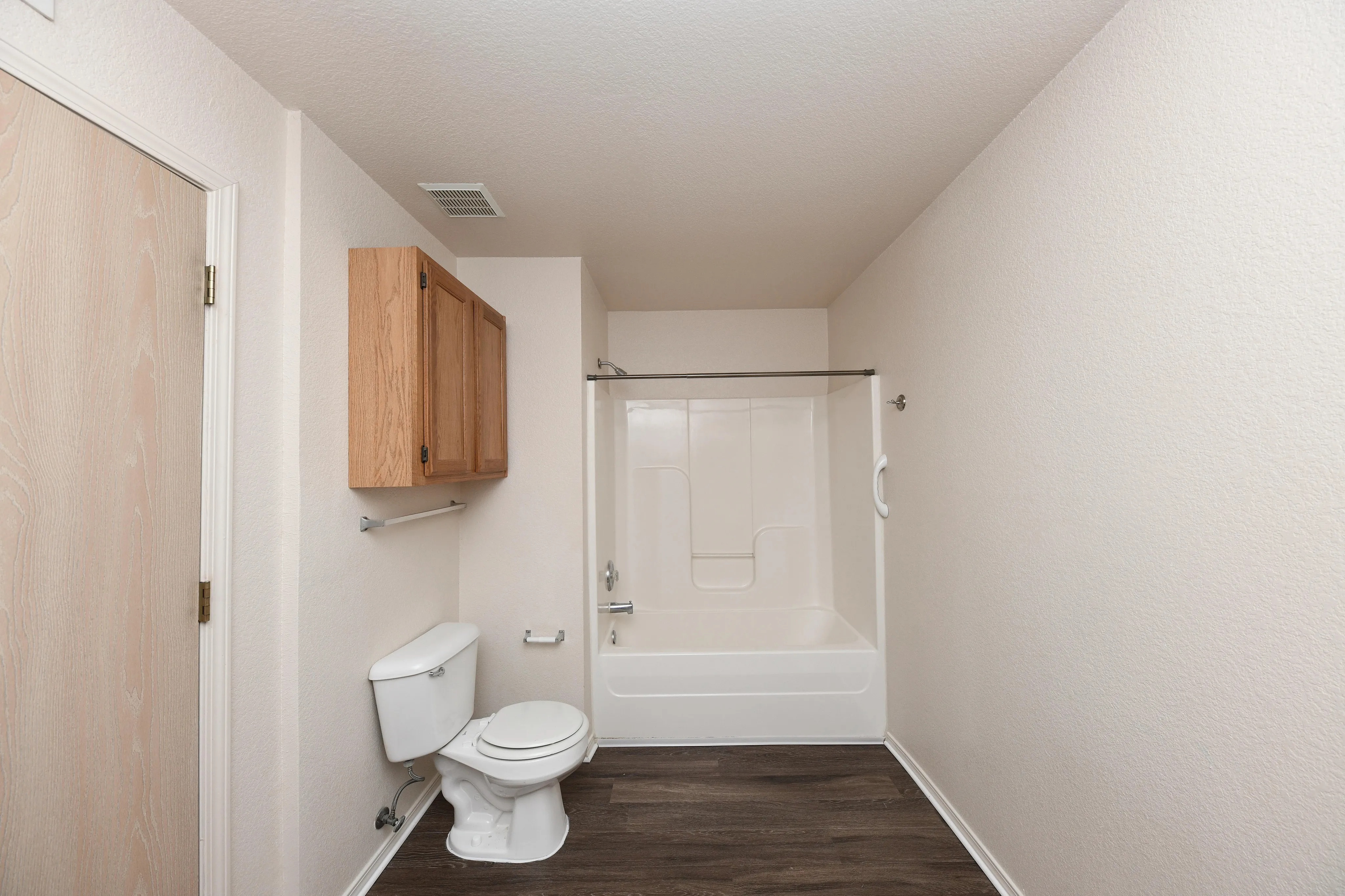 Modern bathroom featuring a sleek bathtub with shower, elegant wooden cabinetry, and stylish dark flooring.