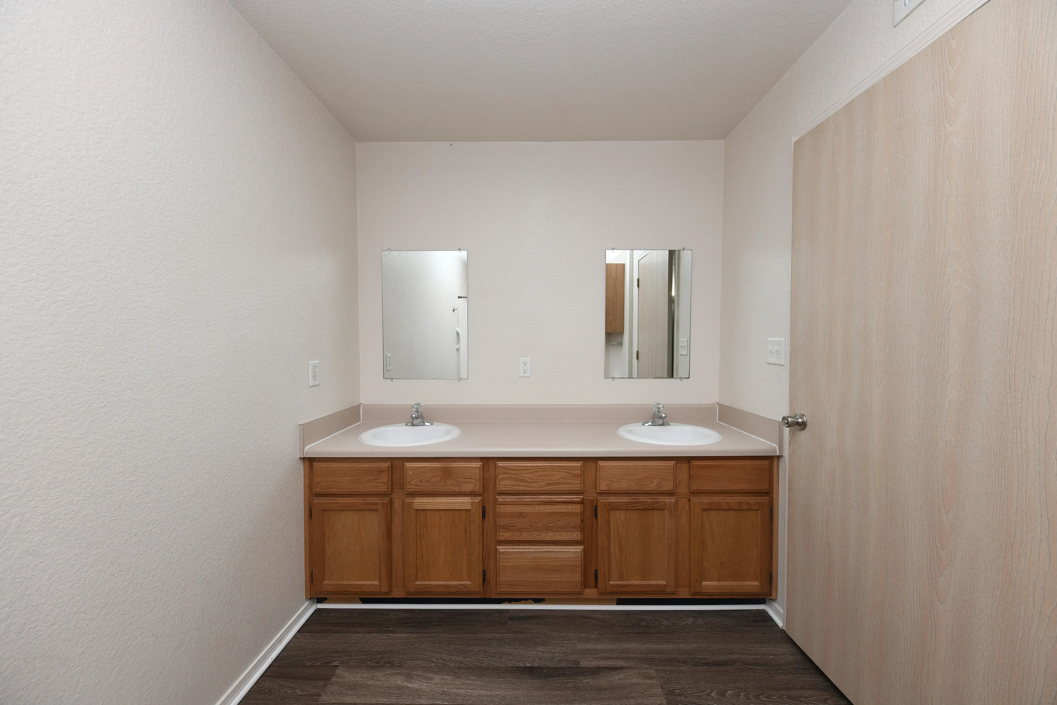 Elegant bathroom with dual sinks, modern wooden cabinetry, and sleek mirrors, offering ample space and functionality.