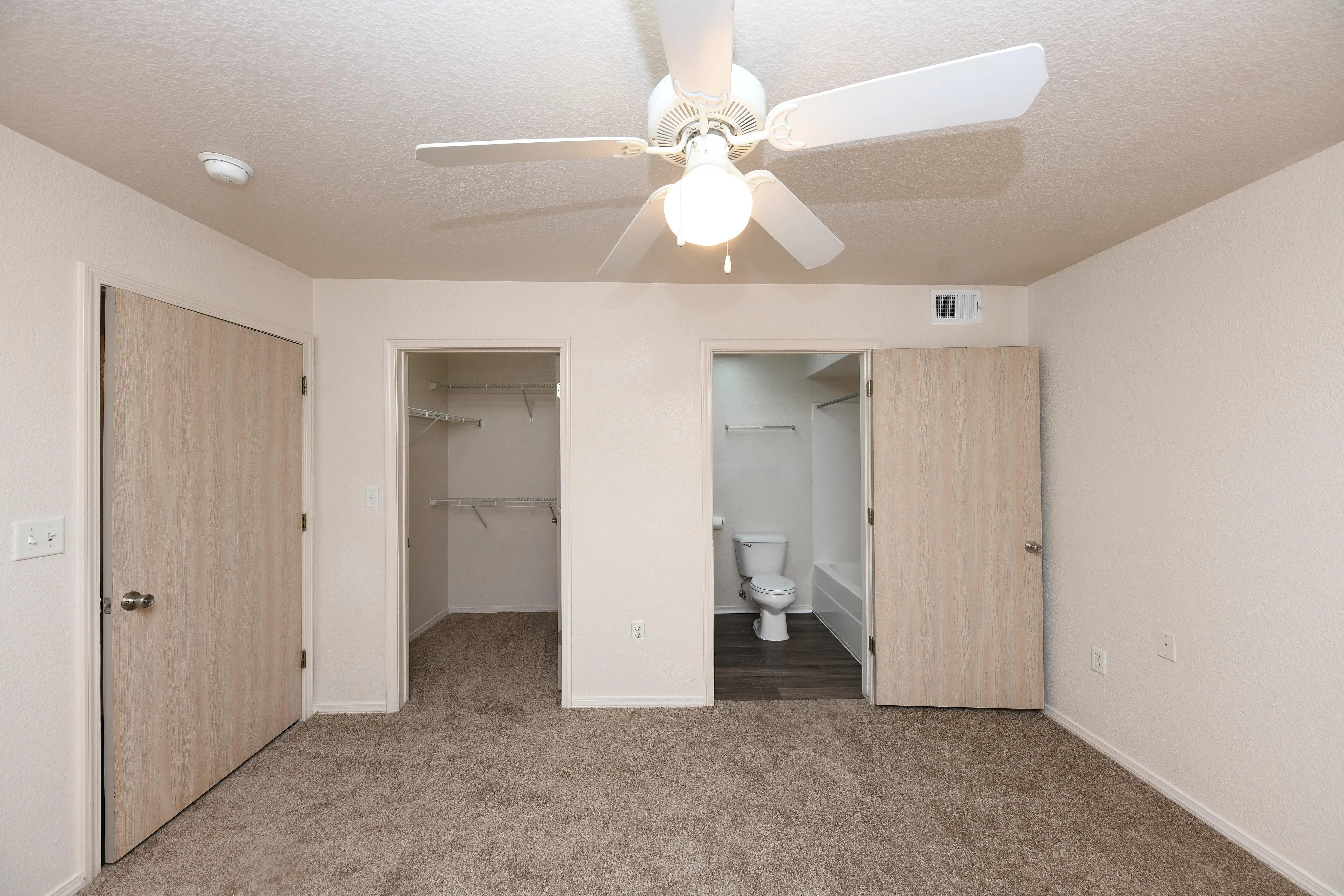 Inviting bedroom with plush carpet, featuring a ceiling fan, spacious walk-in closet, and an en-suite bathroom with modern fixtures.