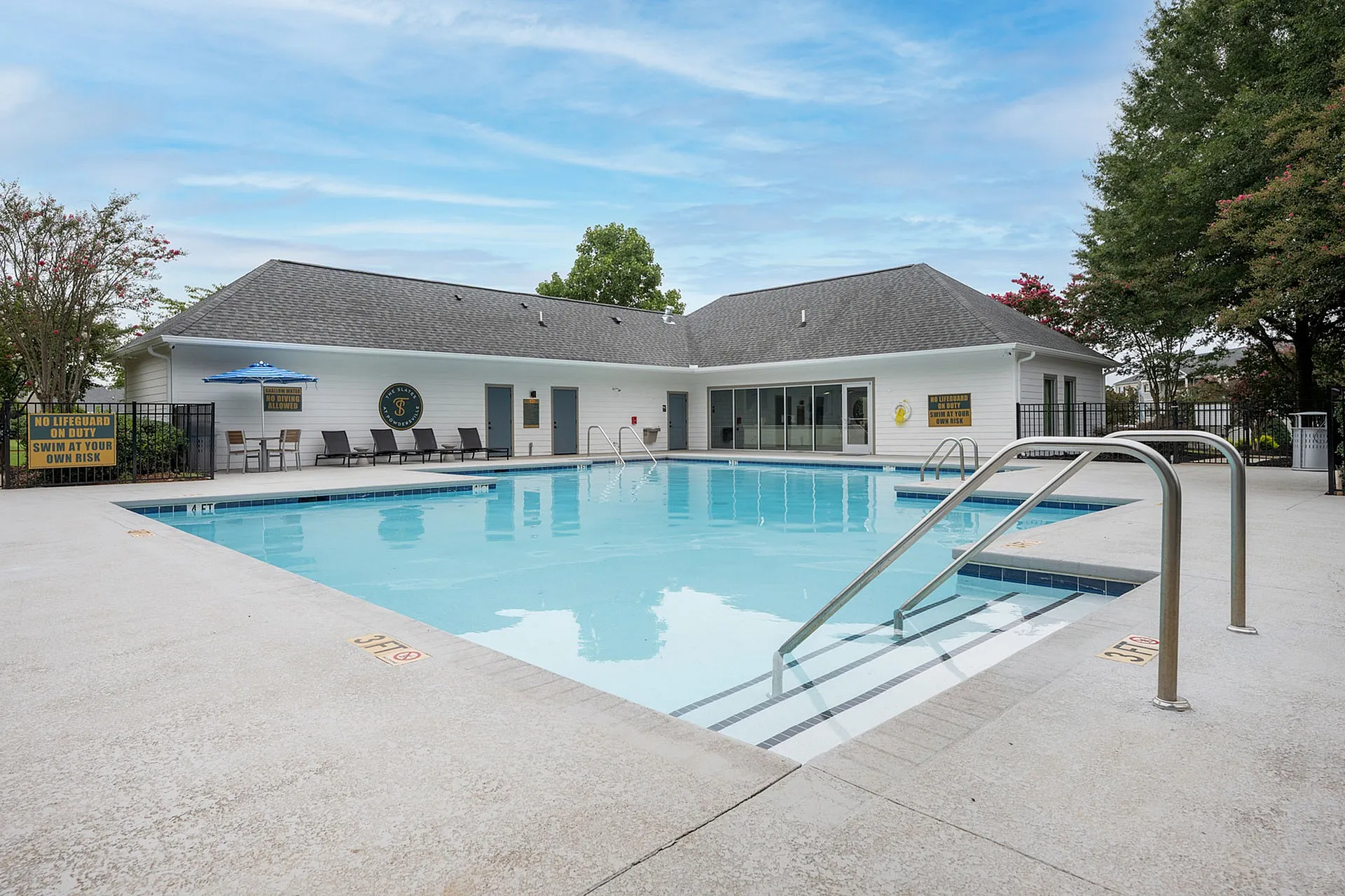 Inviting outdoor pool area with sun loungers and a modern clubhouse, perfect for relaxation and leisure.