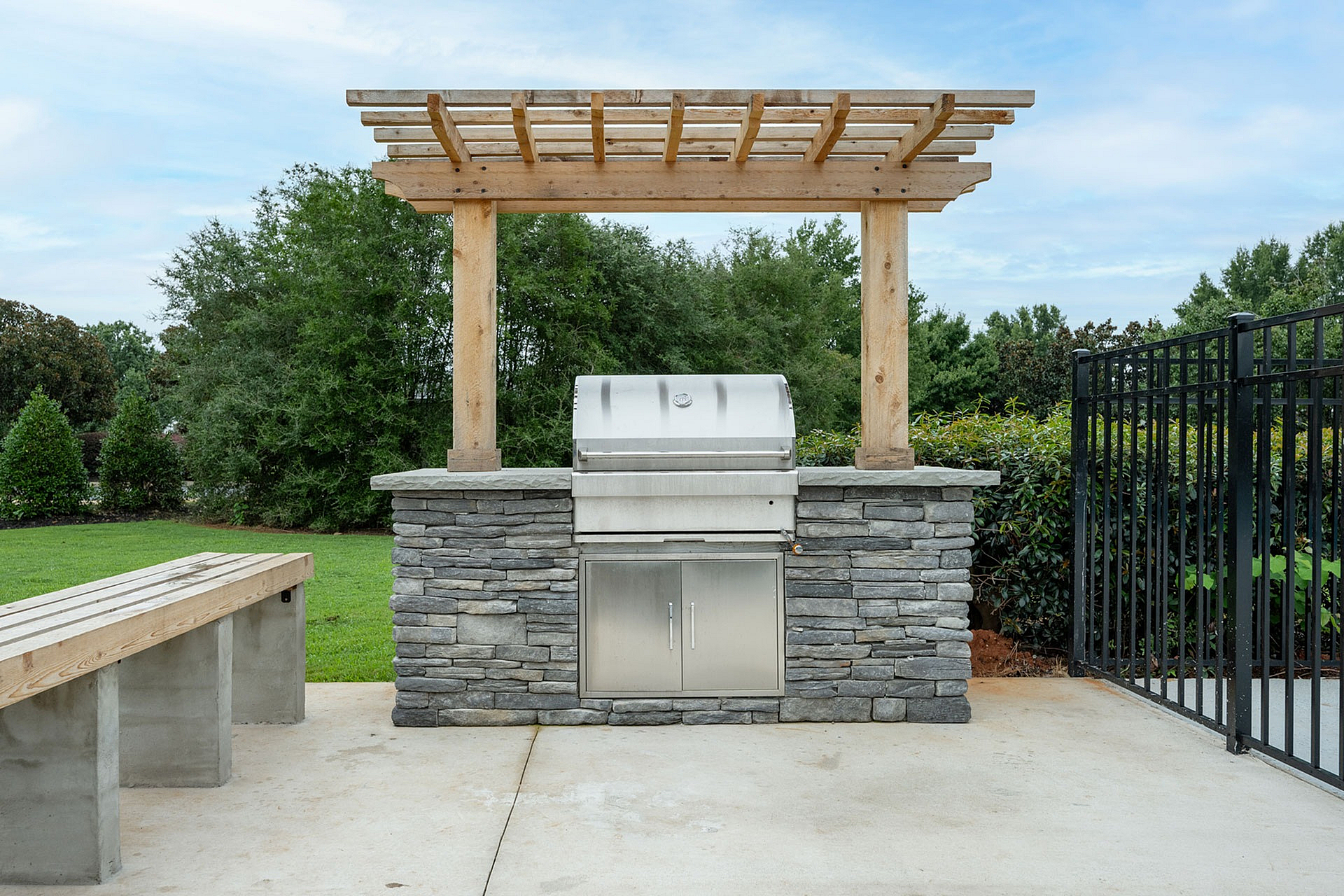 Chic outdoor grilling station with a stone facade and wooden pergola, set against lush greenery.