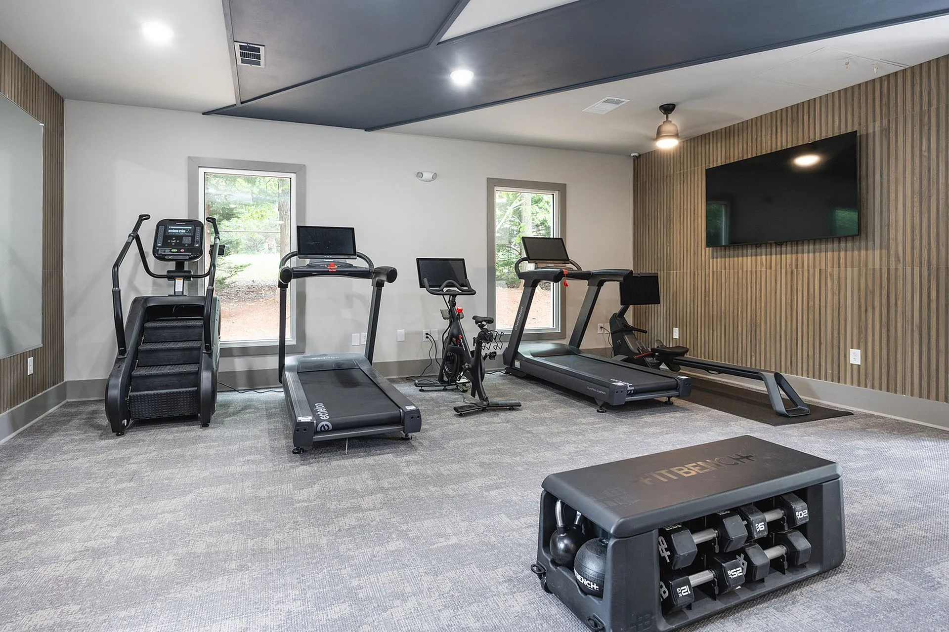 Modern fitness center with sleek cardio machines, including treadmills and a stair climber, alongside a comprehensive FitBench for dynamic workouts.