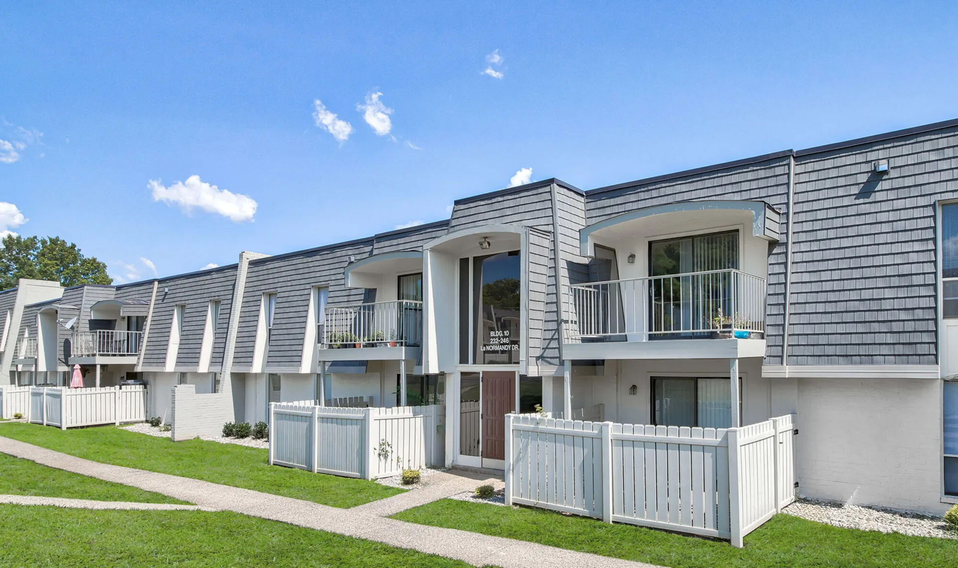 Charming apartment complex with stylish balconies, modern architecture, and inviting fenced areas set against a clear blue sky.