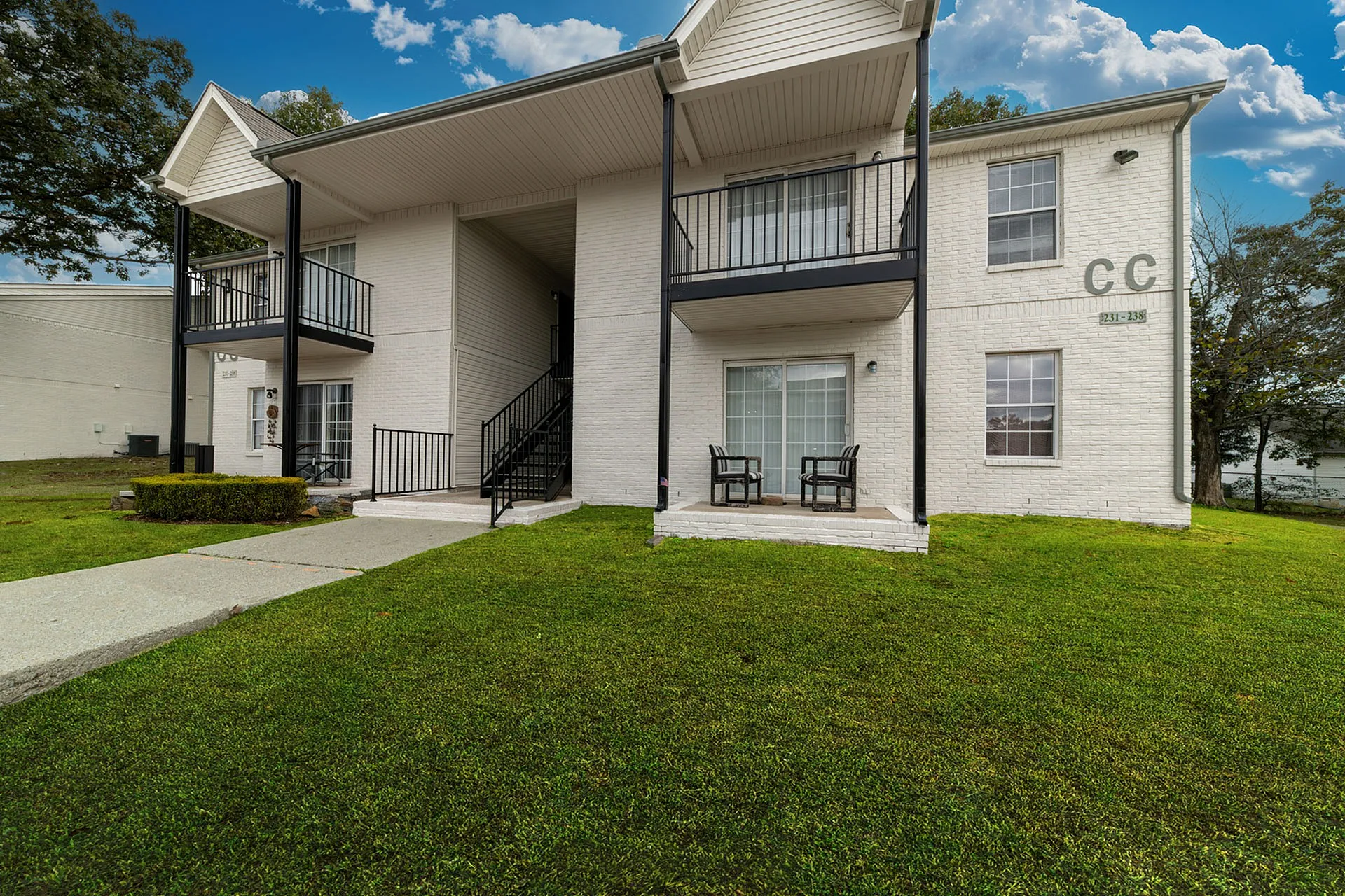 Charming two-story apartment building with white brick facade, featuring balconies and lush green lawn under a brilliant blue sky.