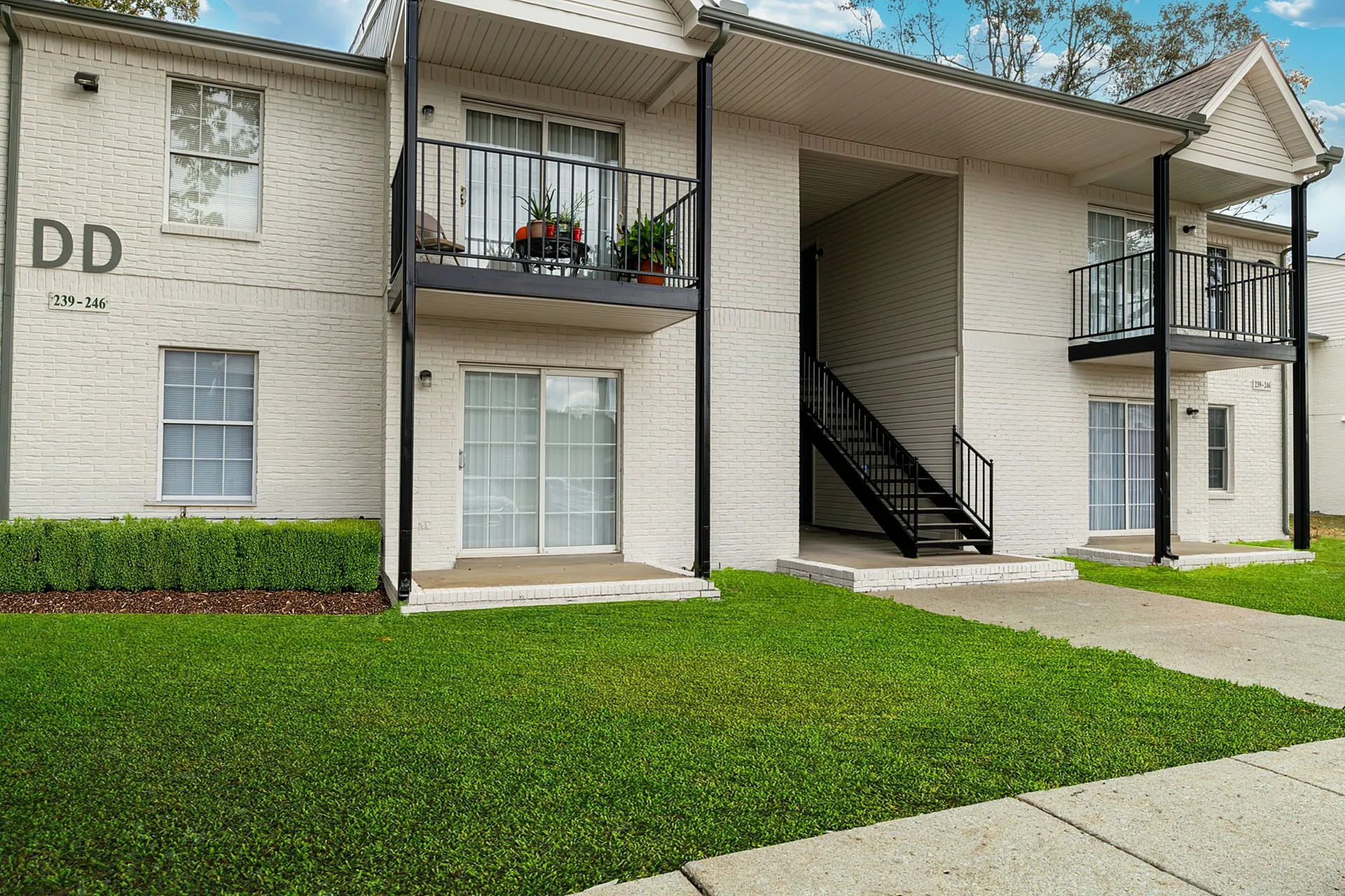 Charming two-story apartment complex with brick exterior, private balconies, and lush green landscaping.