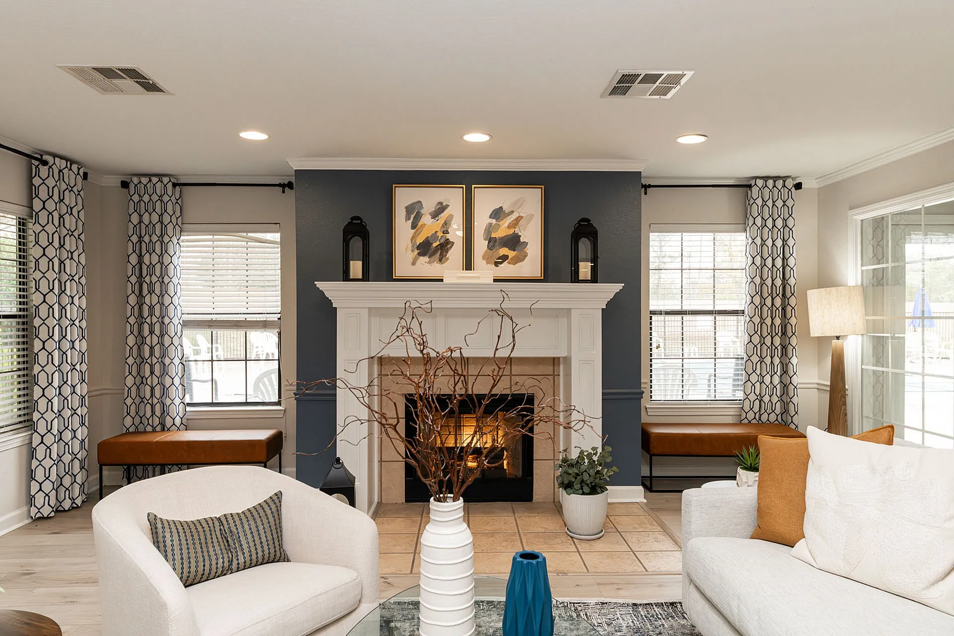 Chic living room with a cozy fireplace, elegant armchairs, large windows with patterned curtains, and modern decor accents.