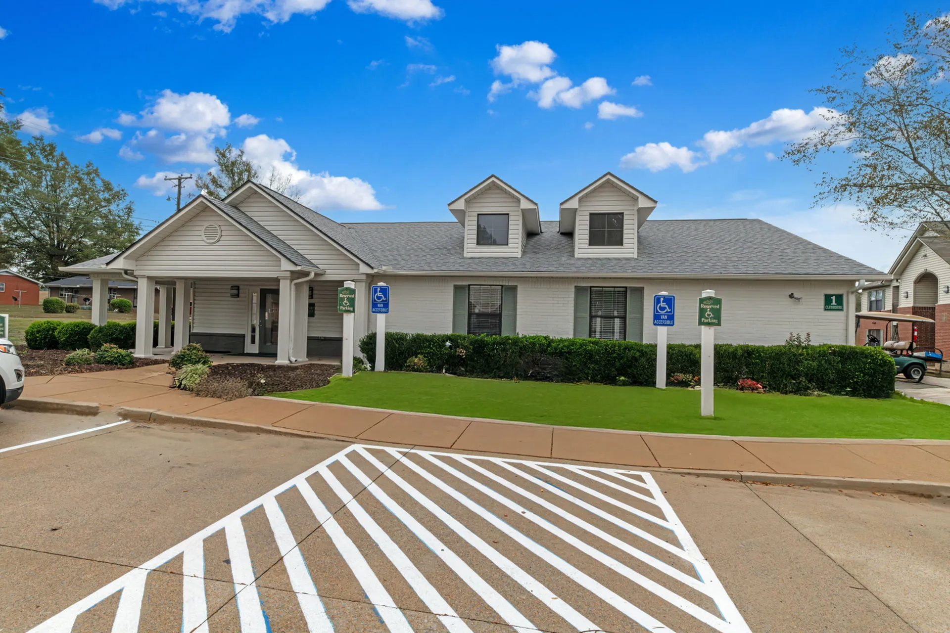 Beautiful suburban home with charming dormer windows, lush green landscaping, and accessible parking, set against a clear blue sky.