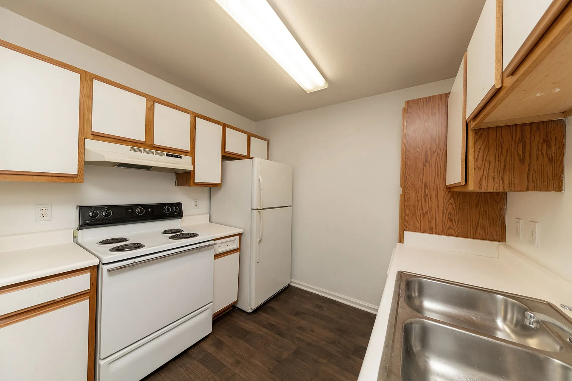 Modern apartment kitchen with sleek dark floors, ample wooden cabinetry, and essential white appliances offering bright and functional space.