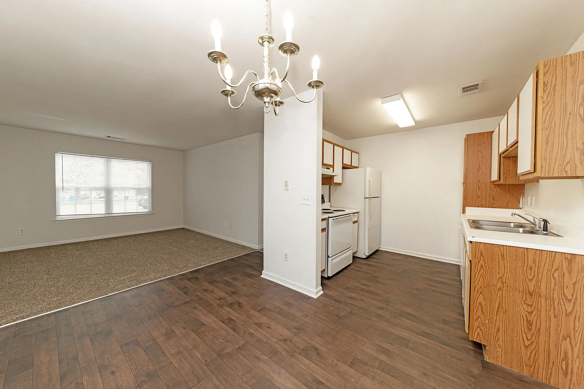 Inviting open-concept apartment with elegant chandelier, cozy carpeted living area, and modern kitchen featuring sleek wood cabinetry.