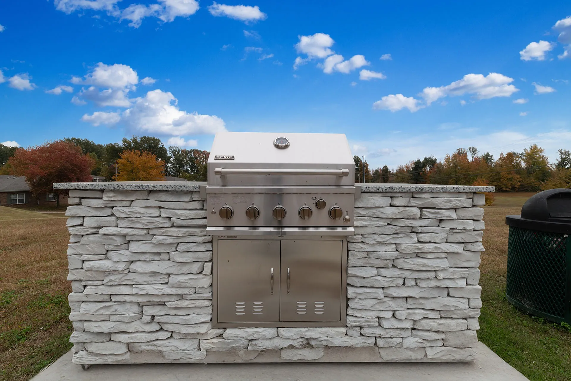Elegant outdoor grill with stylish stone facade, set against a vibrant autumn landscape and blue sky.