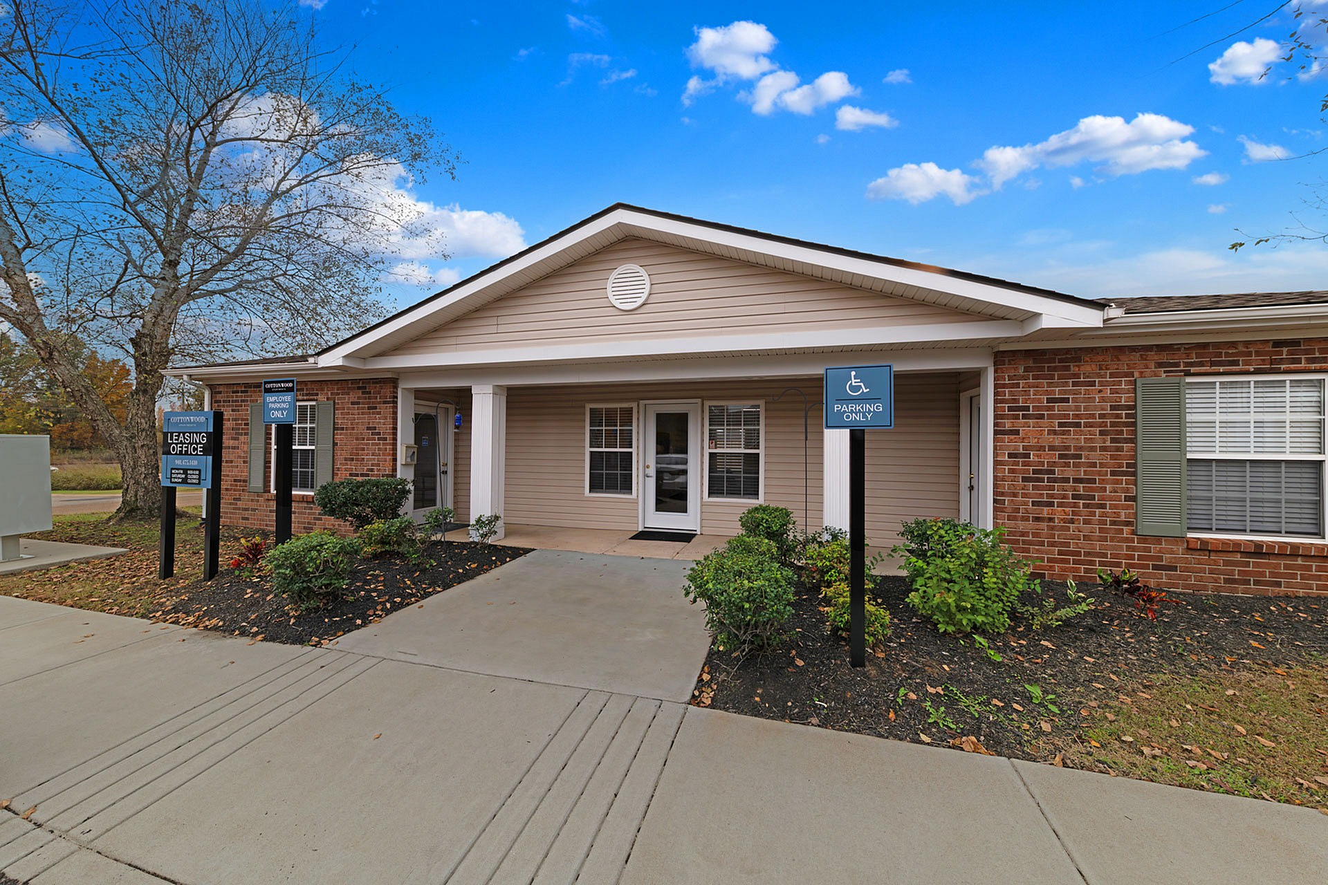 Inviting leasing office entrance with accessible parking, nestled in a beautifully landscaped setting under a vibrant blue sky.