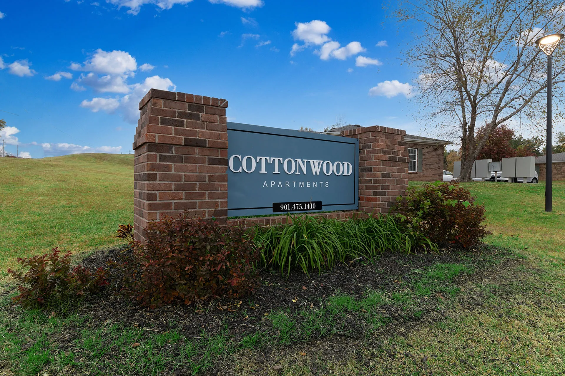 Inviting entrance sign for Cottonwood Apartments, surrounded by vibrant greenery under a clear blue sky.