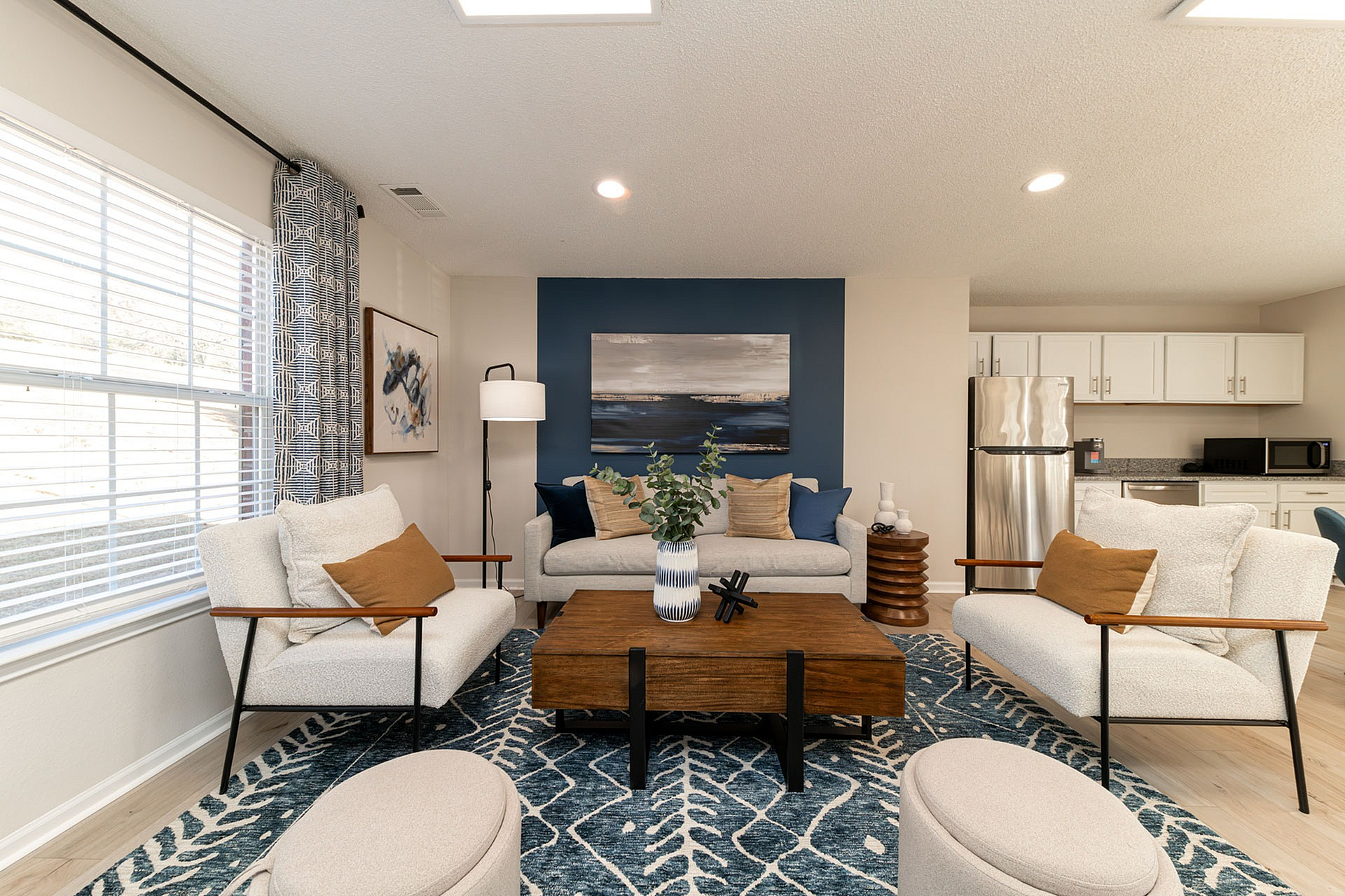 Modern living room with plush seating, stylish decor, and a sleek kitchen featuring stainless steel appliances in the backdrop.