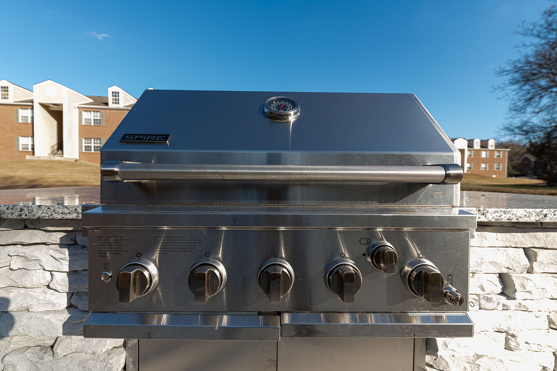 Modern outdoor stainless steel grill set against a picturesque apartment building backdrop, ideal for entertaining and enjoying sunny days.