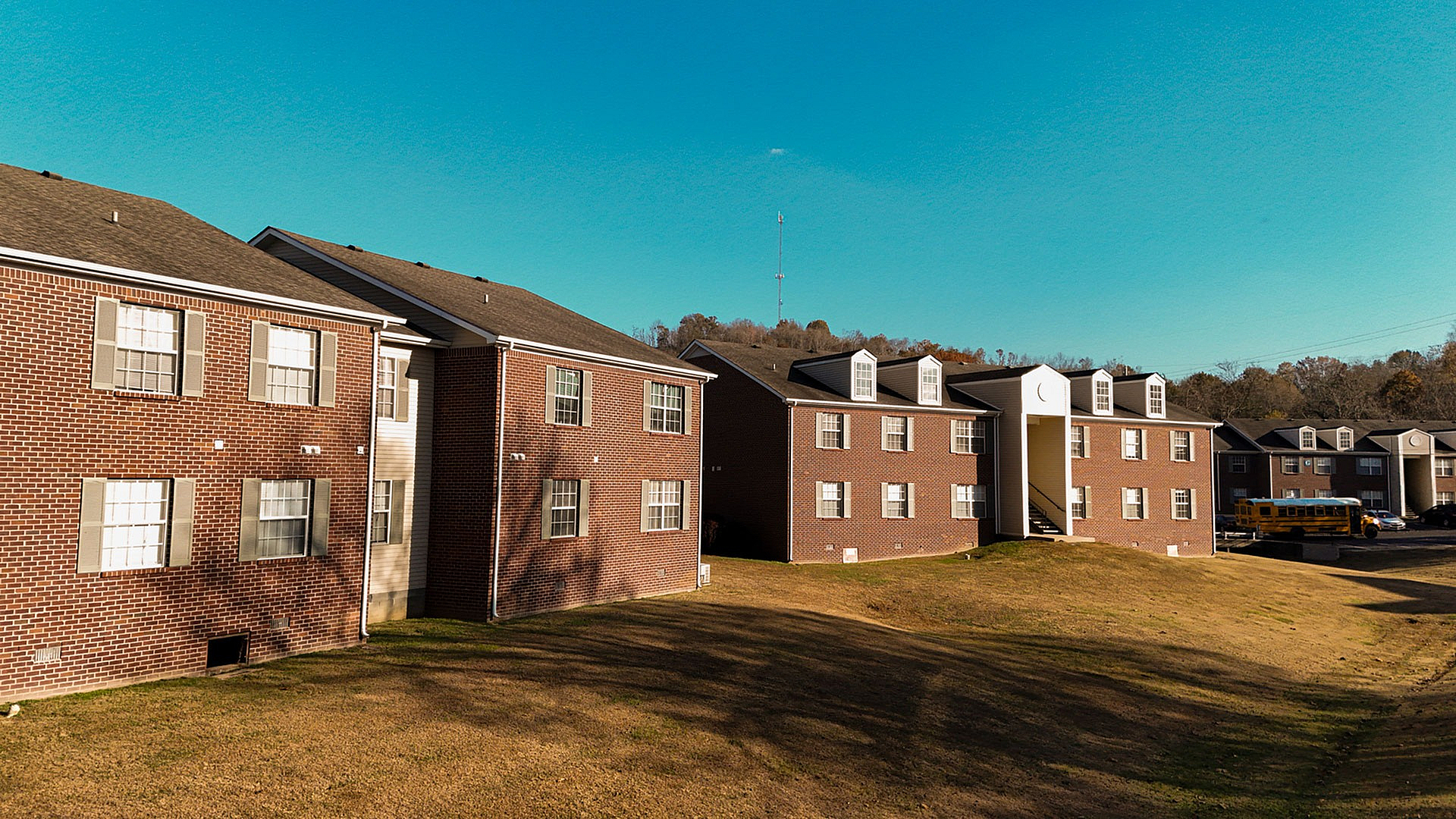 Charming brick apartment buildings under a clear blue sky, offering a serene living environment with lush grassy areas.