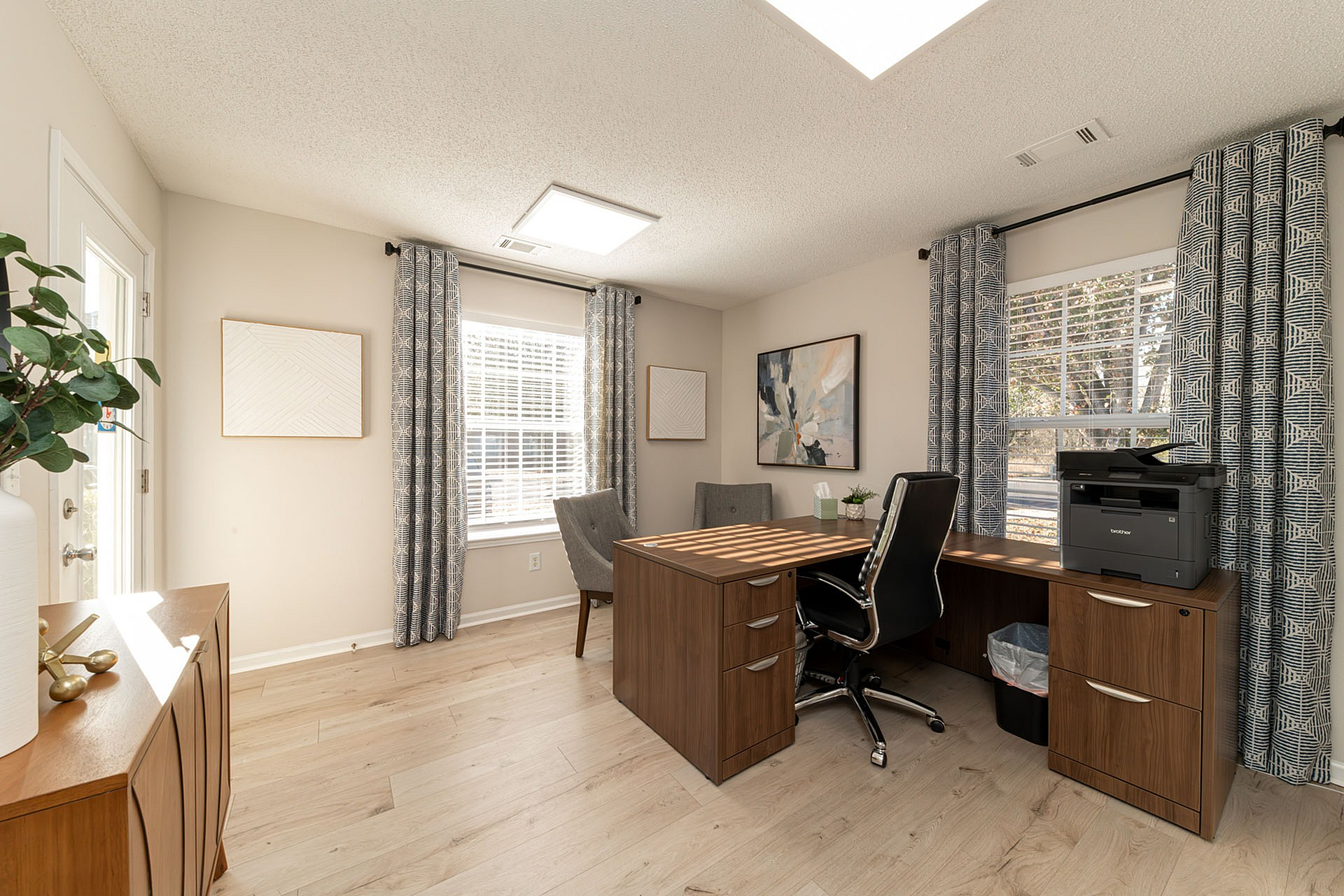 Bright and modern home office with sleek wooden desk, elegant decor, and ample natural light.