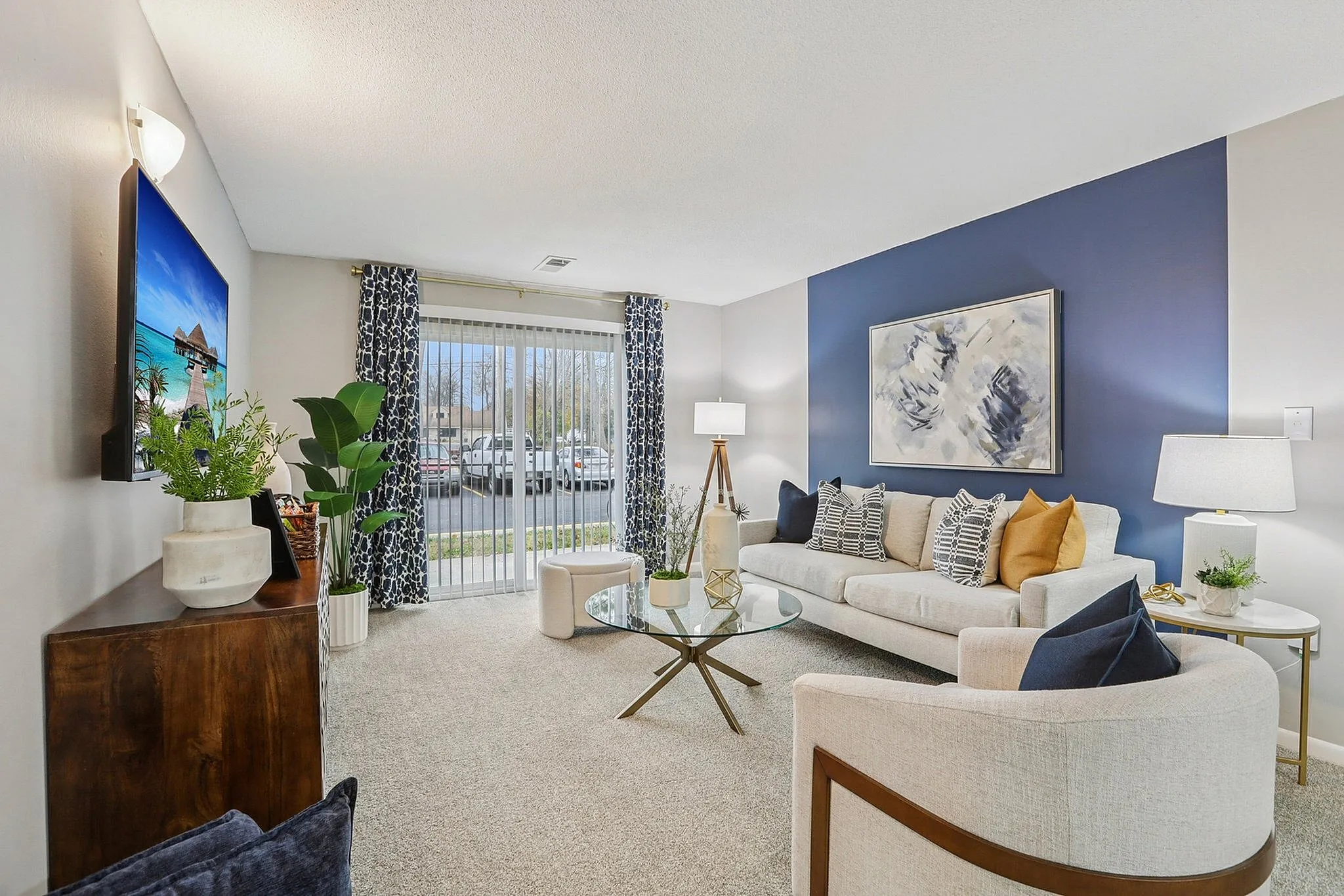 Elegant living room boasting modern decor with a cozy sofa, abstract artwork, and a vibrant blue accent wall. Large window with chic drapes invites ample natural light.