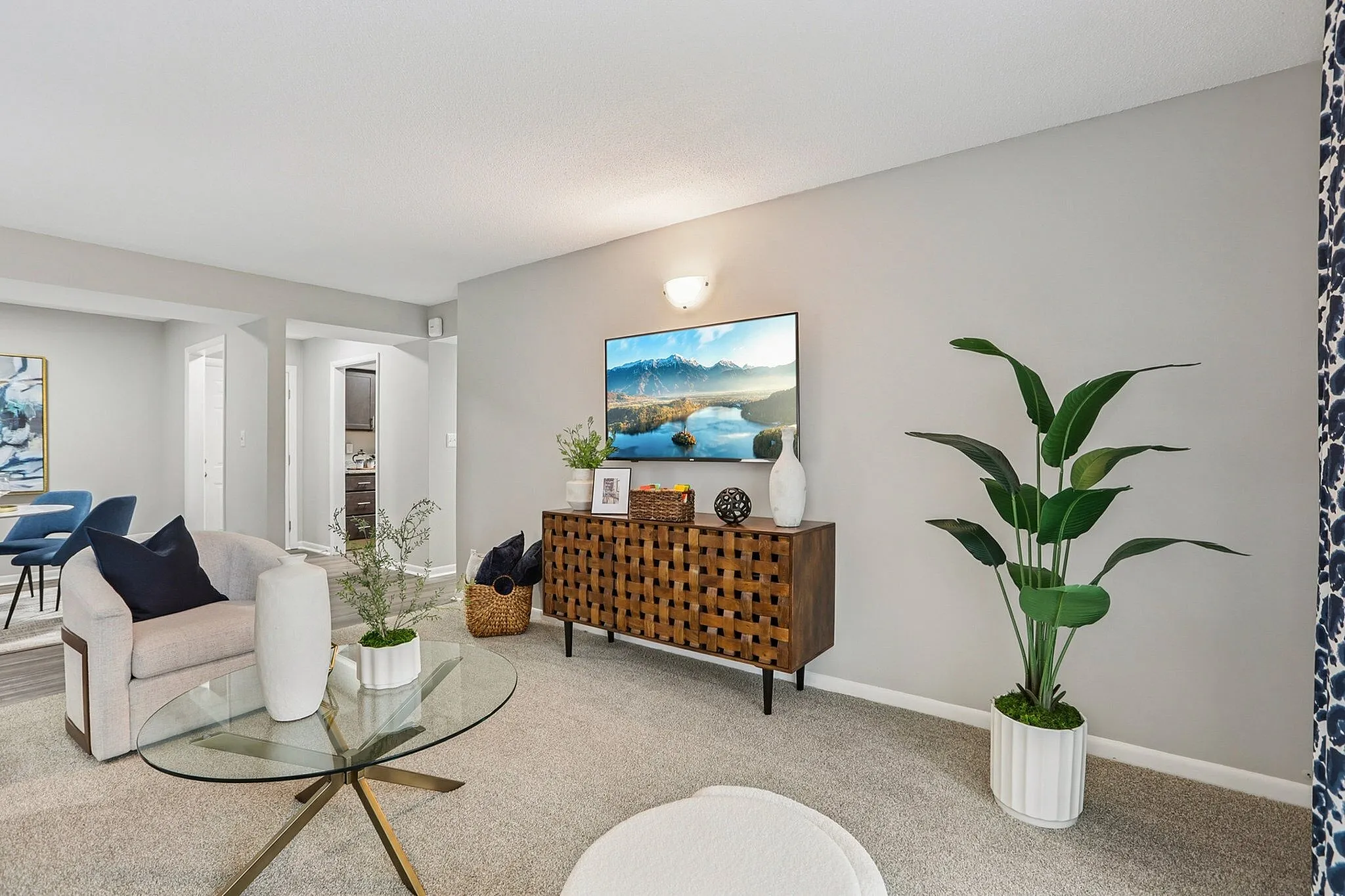 Elegant living room with modern decor, featuring a plush chair, glass coffee table, and stylish sideboard with art piece and vibrant indoor plant.