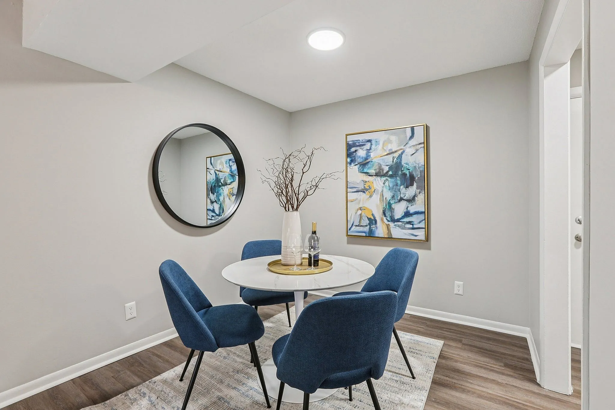 Elegant dining nook featuring a round table, blue chairs, and chic modern decor, complemented by stylish artwork and a sleek round mirror.