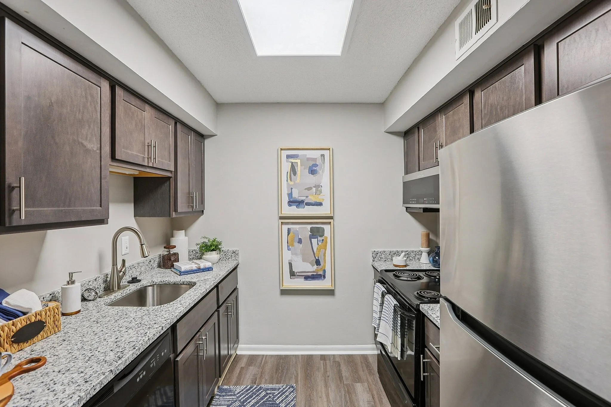 Contemporary galley kitchen with sleek granite countertops, modern dark wood cabinetry, and stainless steel appliances under soft natural light.