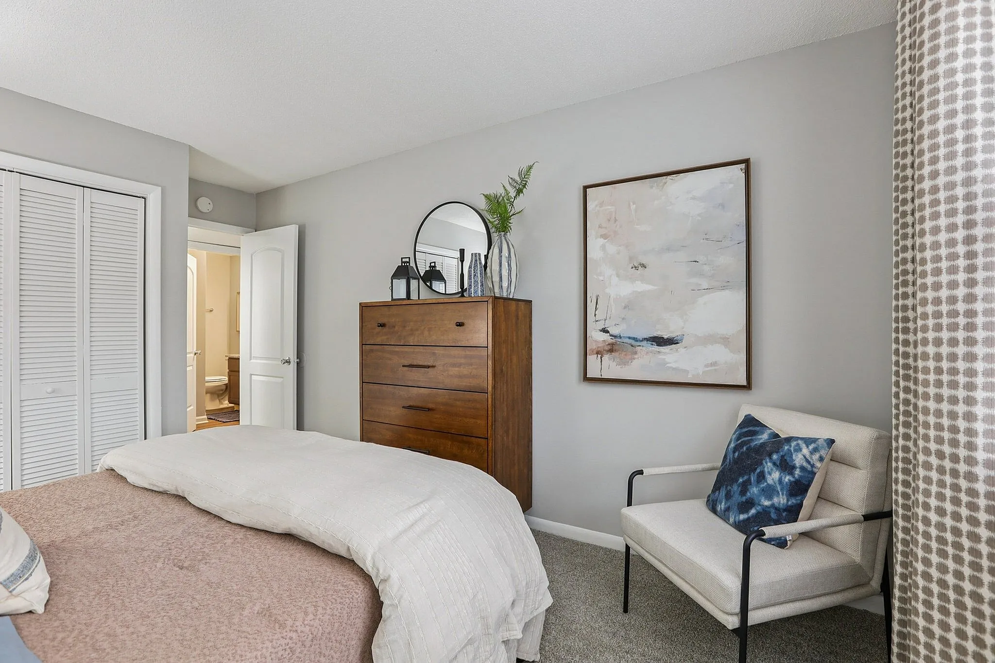 Inviting bedroom with cozy bed, stylish dresser, chic art piece, and comfortable armchair, embodying modern elegance.
