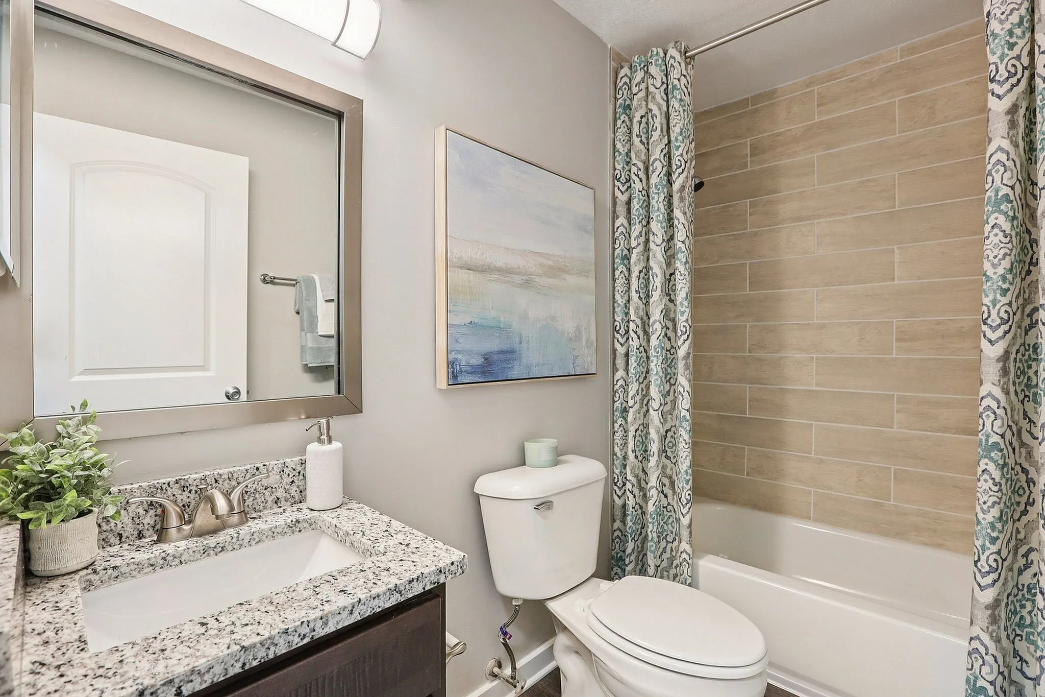 Modern bathroom featuring a granite countertop, elegant wall art, and stylish patterned shower curtain with earthy tones.