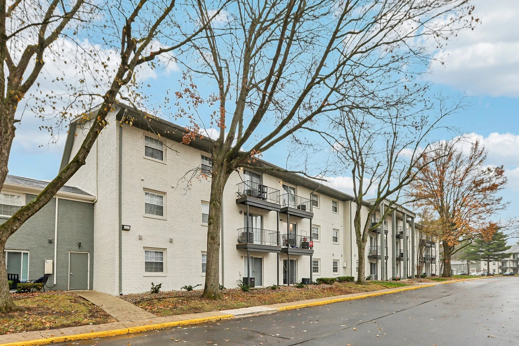 Charming apartment complex with modern balconies and scenic tree-lined surroundings under a clear sky.