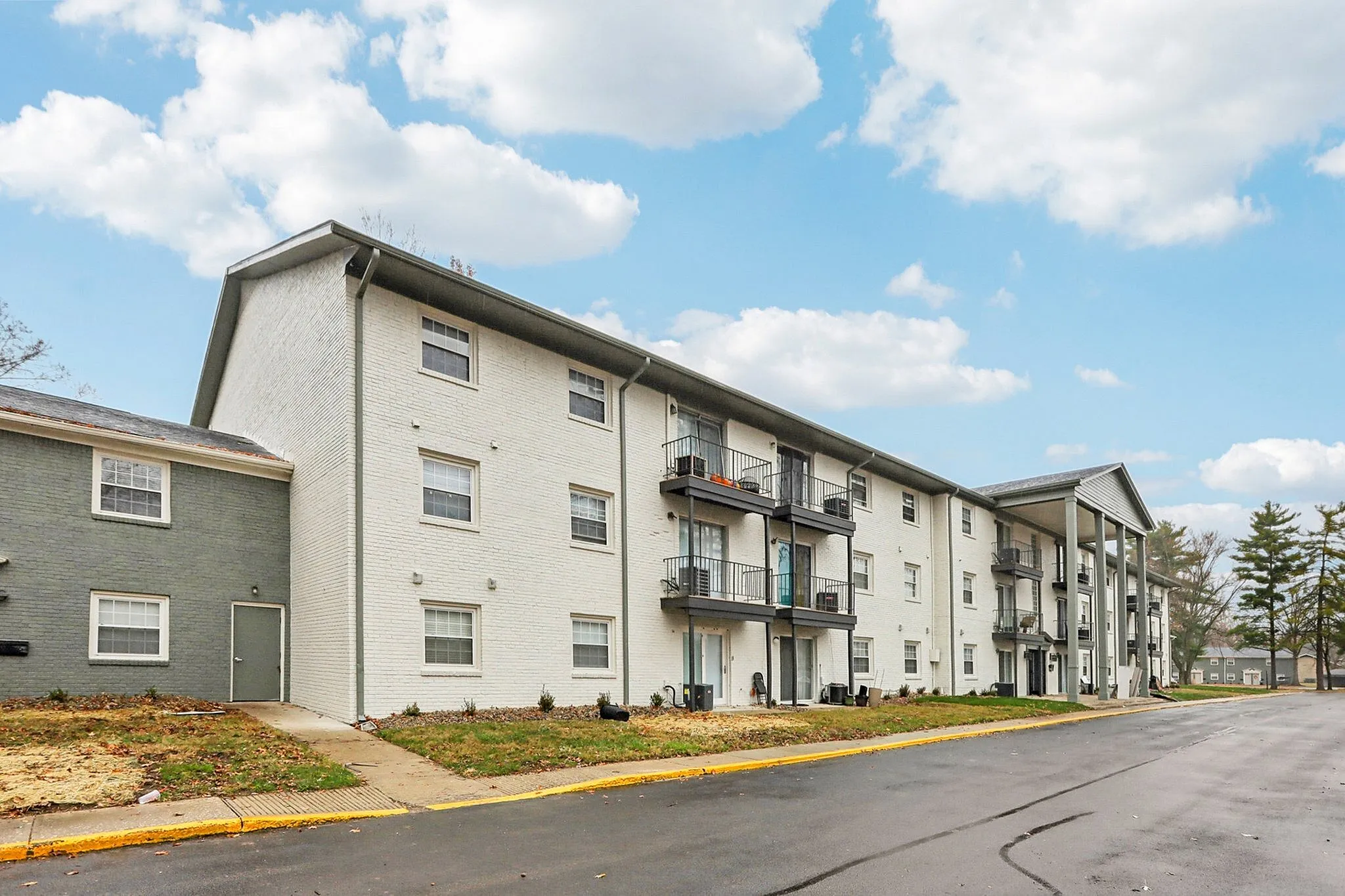 Charming mid-rise apartment building with balconies, surrounded by a well-maintained lawn and clear skies.