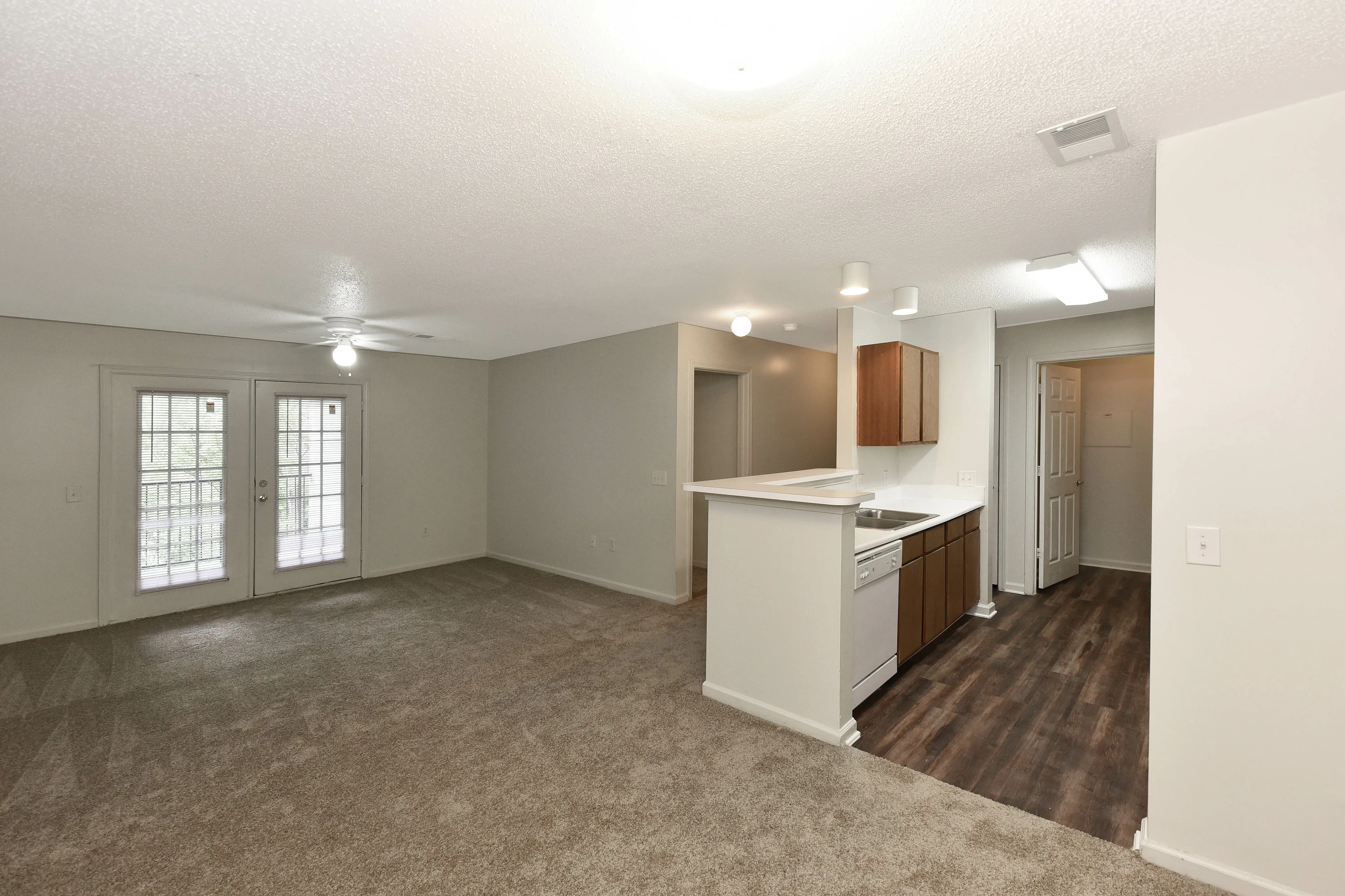 Bright and open living space featuring plush carpeting, modern kitchen with wood cabinets, and large glass doors leading to a serene outdoor view.