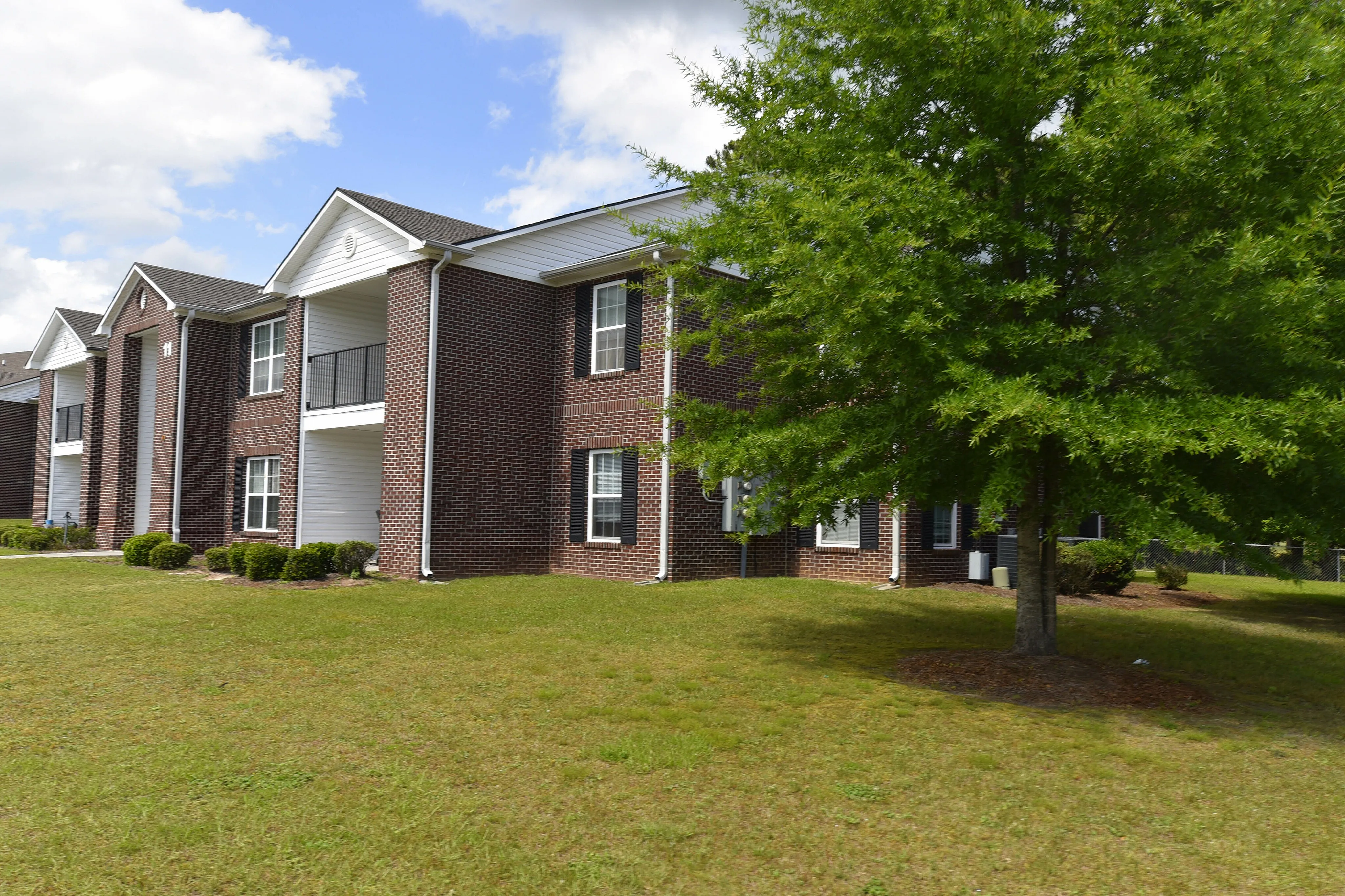 Charming red brick apartment building with manicured green lawn and lush trees, promising tranquil and stylish living.