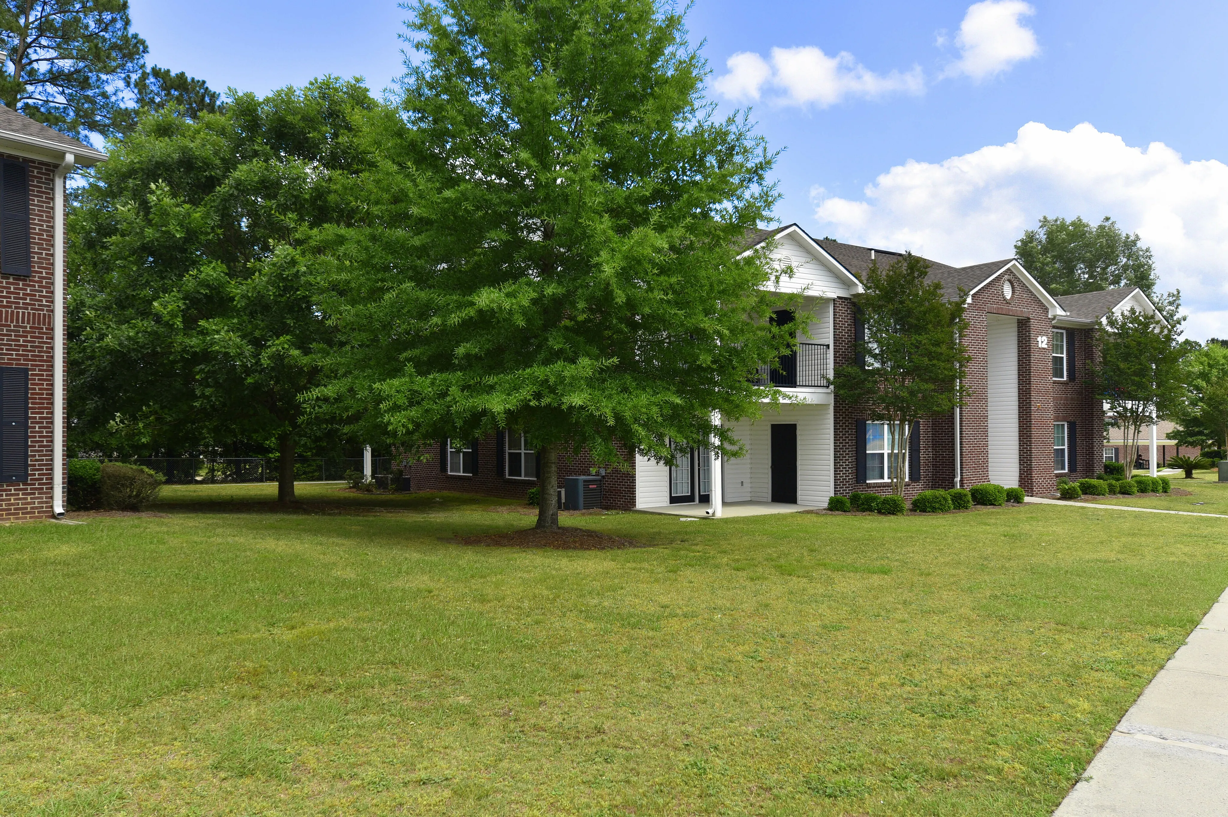 Charming brick apartment complex surrounded by lush green lawns and trees under a bright blue sky.