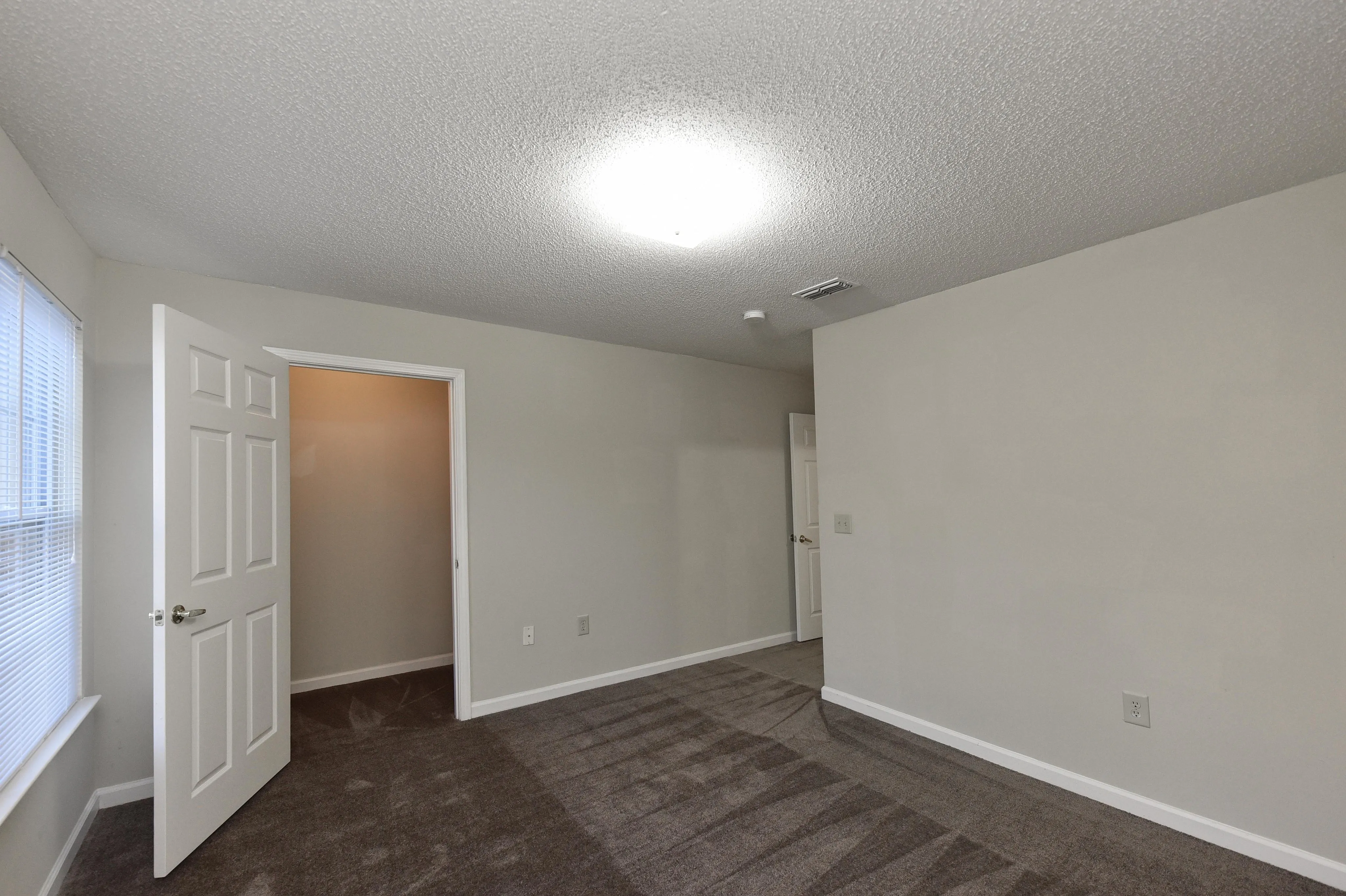 Inviting bedroom with plush carpet, soft neutral walls, and ample natural lighting, perfect for a cozy retreat.