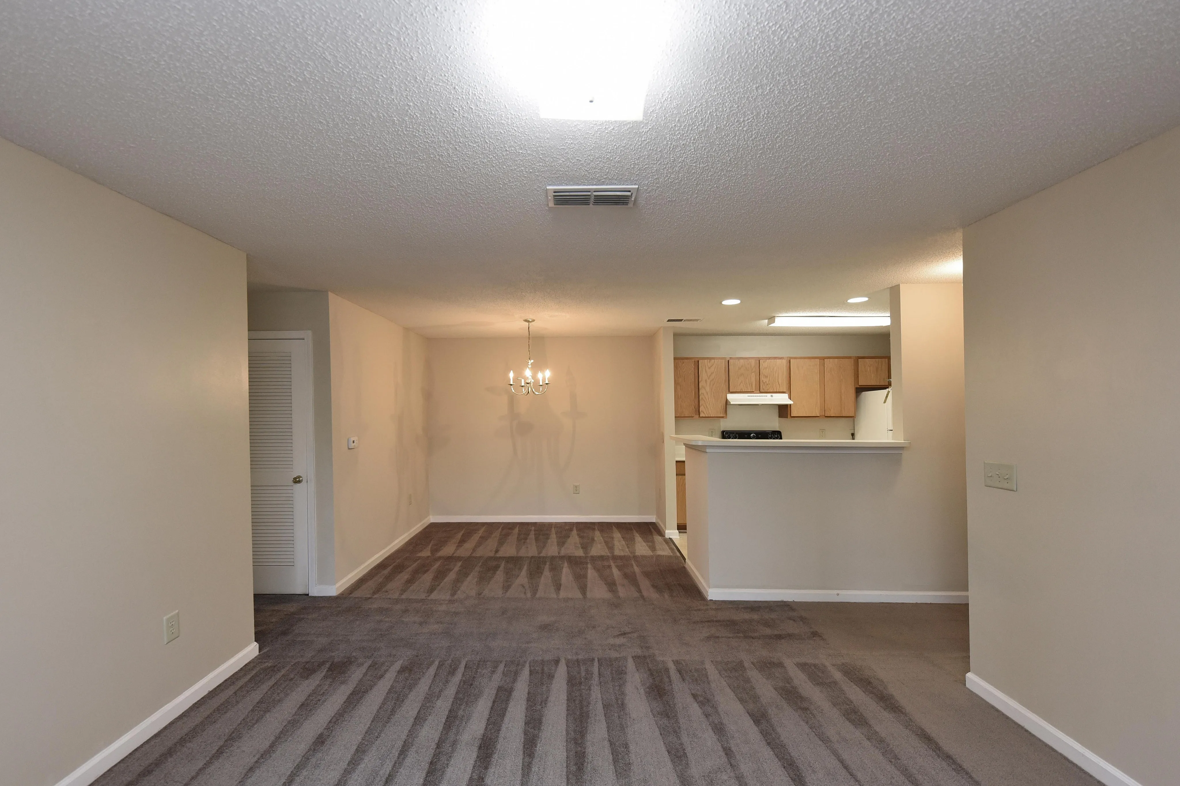 Bright and welcoming open-concept living space with elegant chandelier and modern kitchen with ample cabinetry.