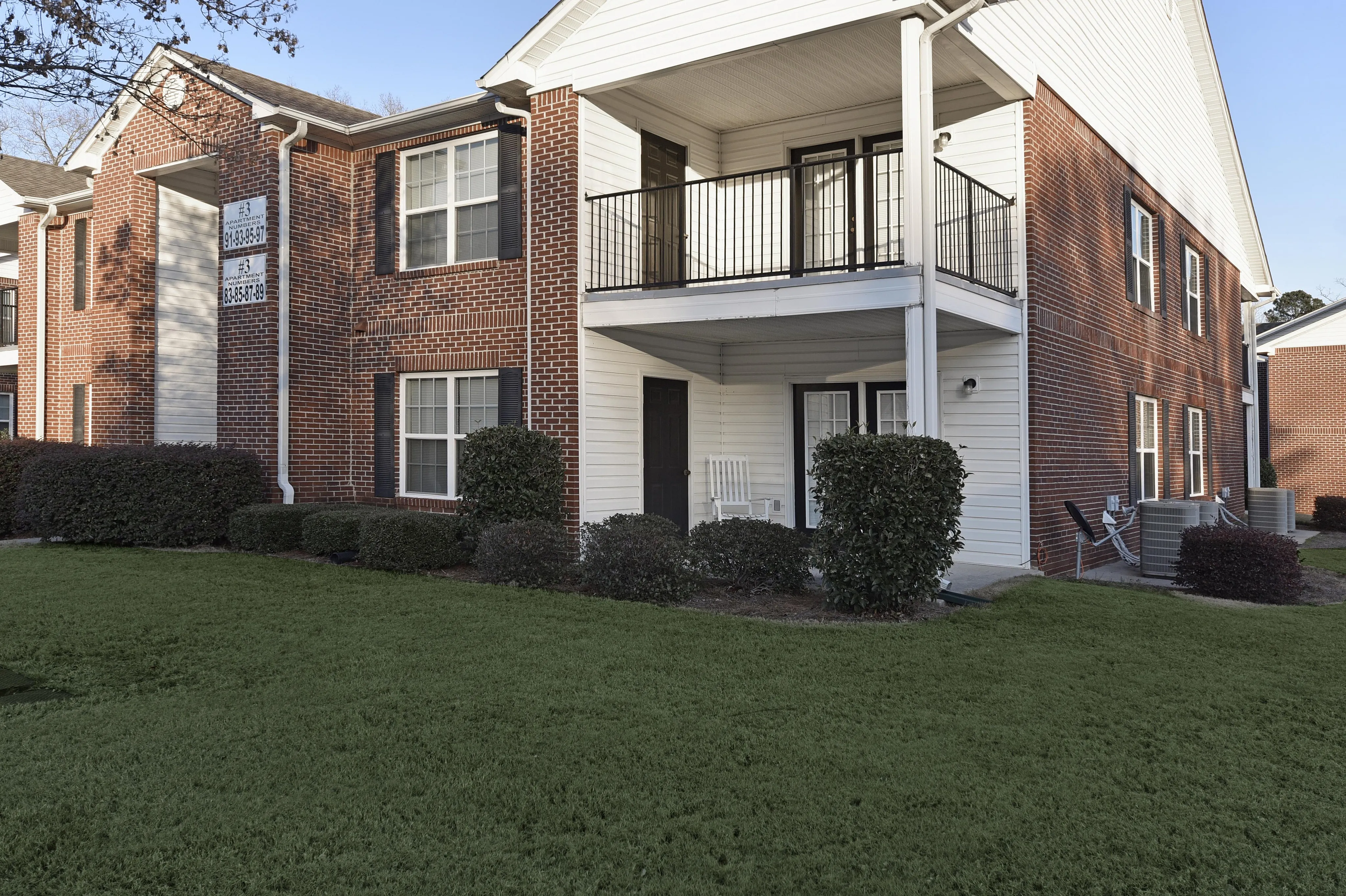 Charming brick apartment building with lush green lawn, featuring inviting balconies and modern architecture.