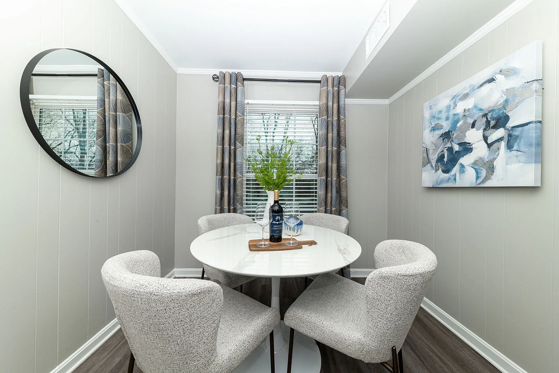 Chic dining nook showcasing a round modern table with elegant grey chairs, complemented by a stylish abstract painting and vibrant greenery.